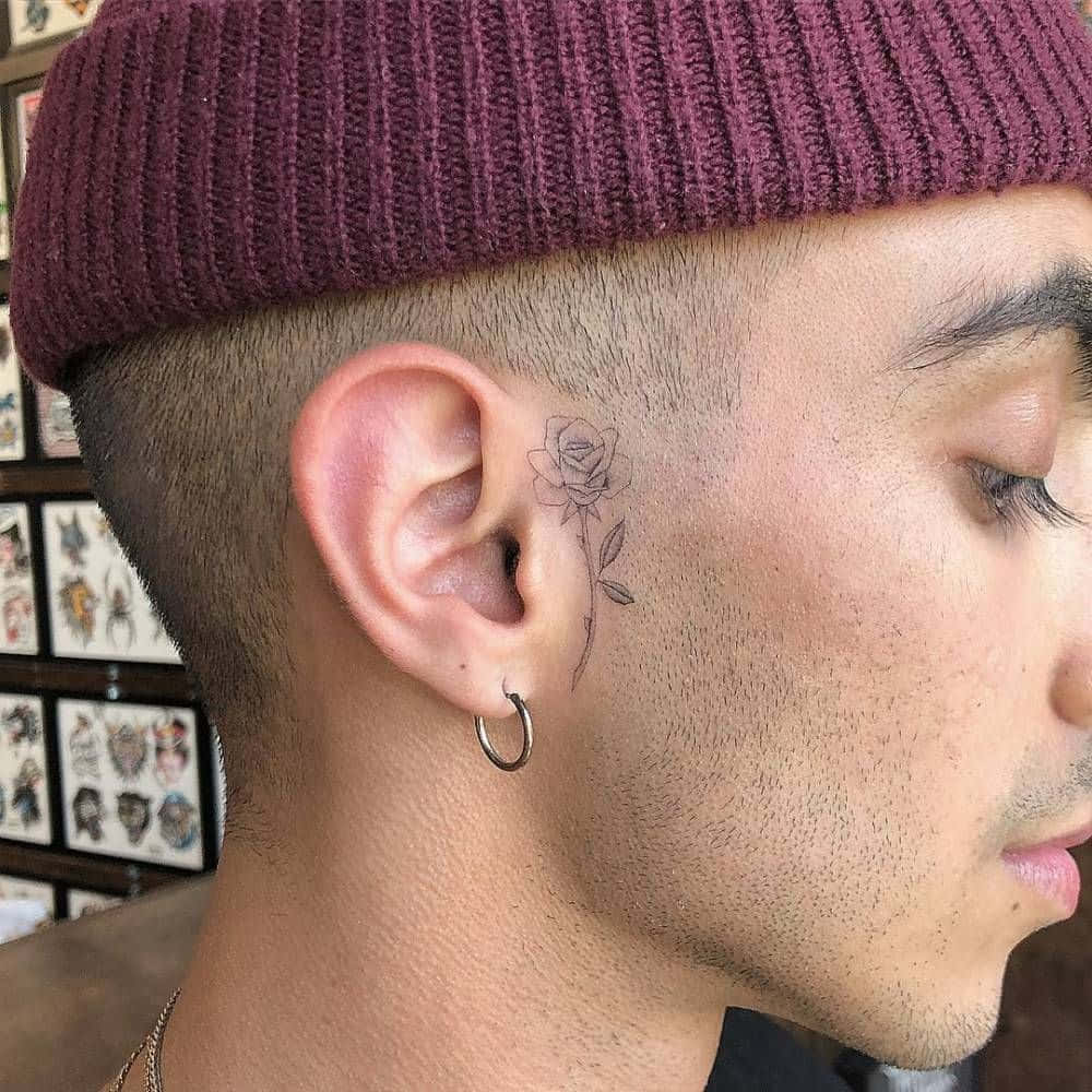 Face Tattoo 桌布 壁紙 — 男士側面特寫，耳後有精緻玫瑰刺青，戴著栗色無邊帽和圓環耳環。