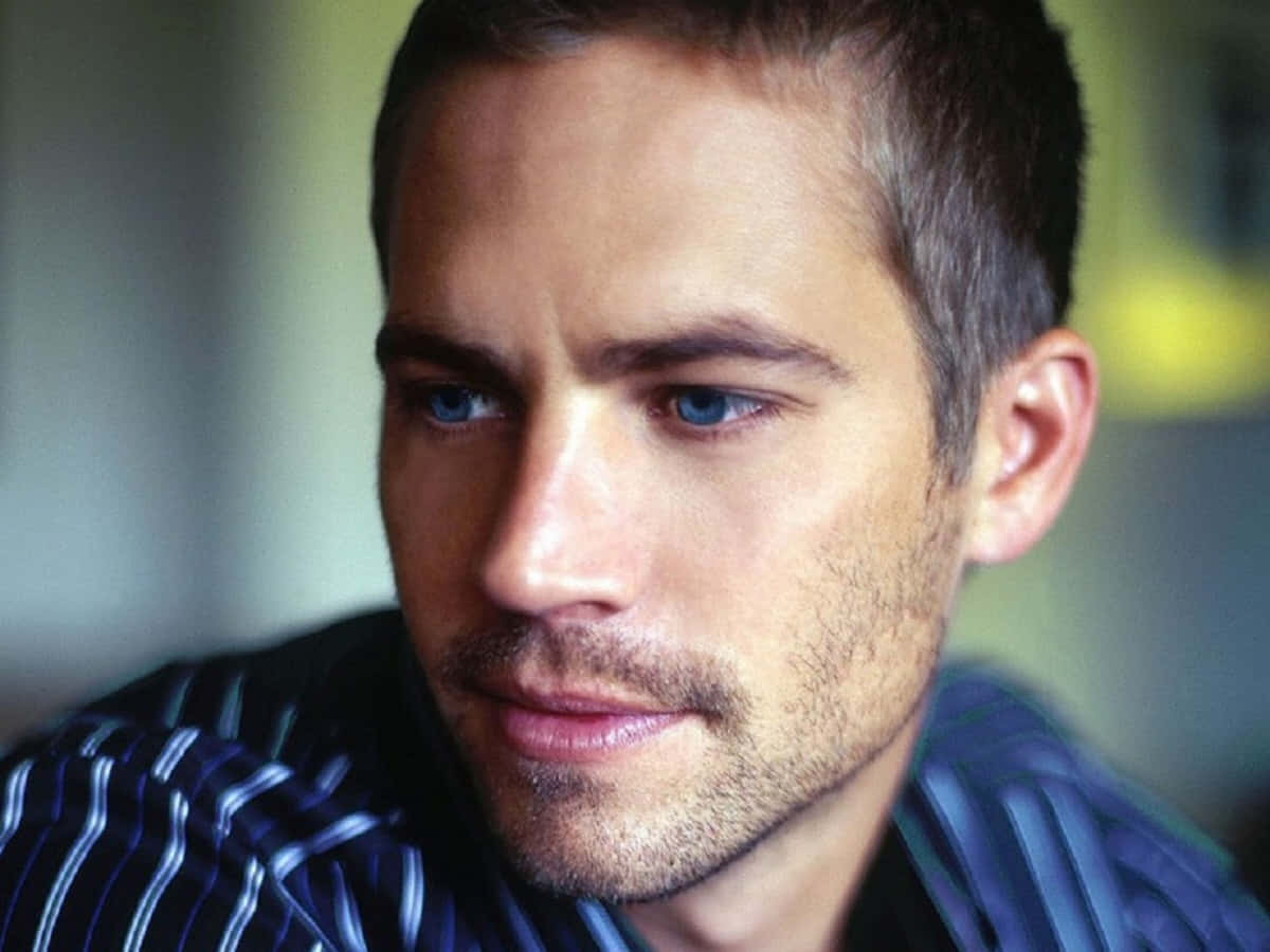 Paul Walker 桌布 壁紙 — 男士特寫肖像，擁有強烈的藍色眼睛和鬍渣，身穿條紋襯衫，背景模糊。