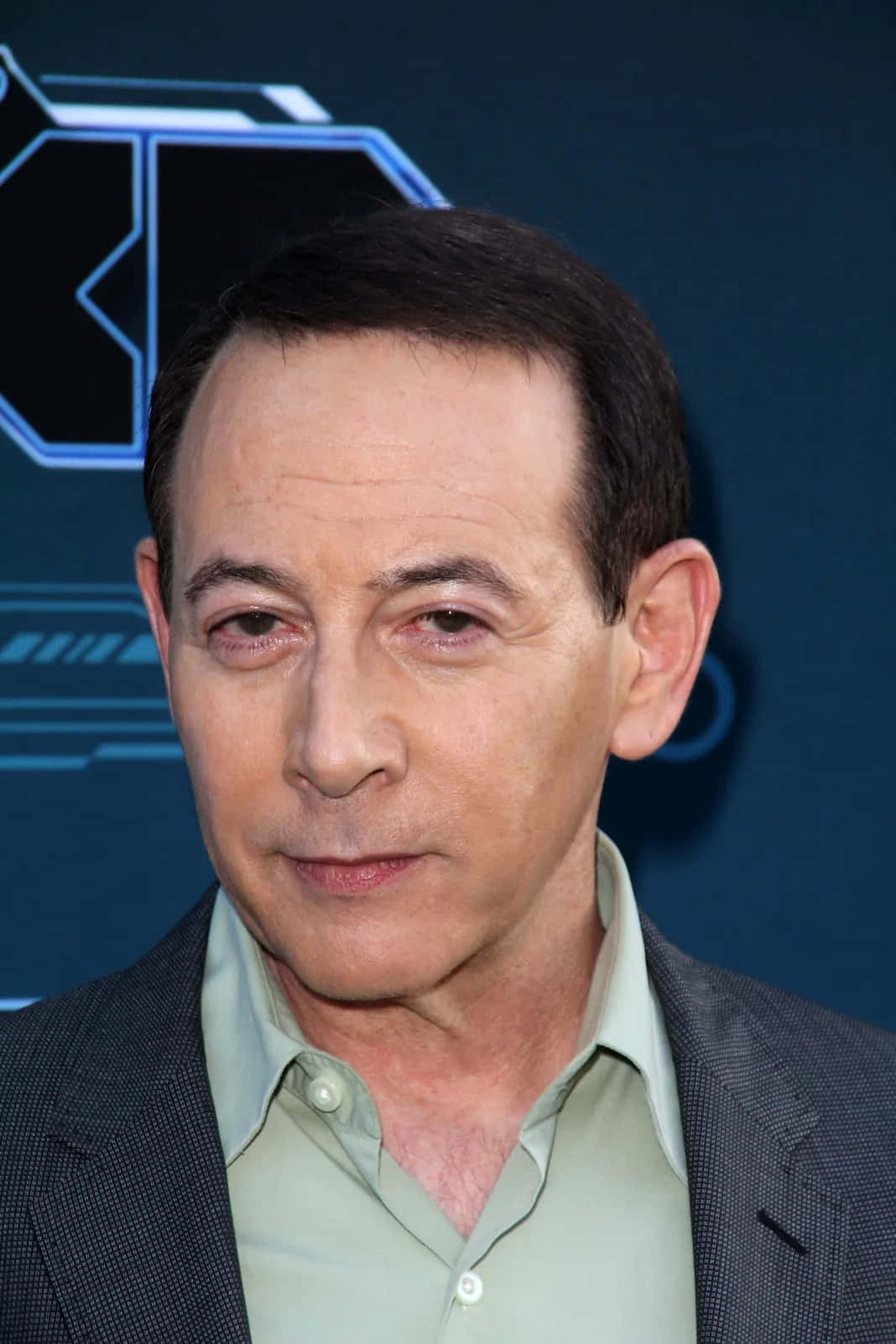 Paul Reubens 桌布 壁紙 — 男士身穿西裝和淺色襯衫的 close-up 肖像，背景為藍色科技主題。