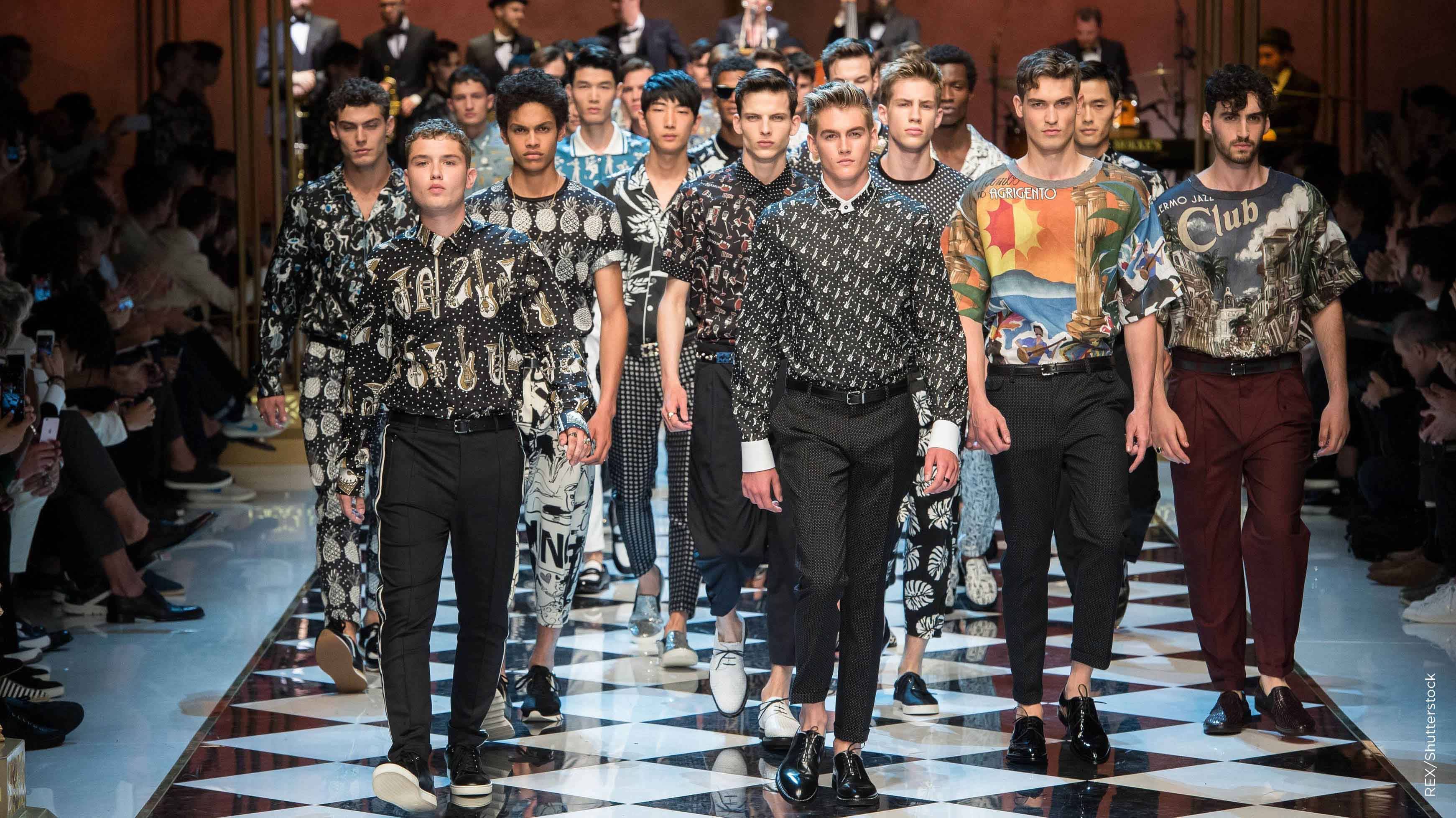 Runway 桌布 壁紙 — 男模特兒自信地走在格子圖案的時裝伸展台上，穿著大膽圖案襯衫和深色褲子，在明亮燈光下。