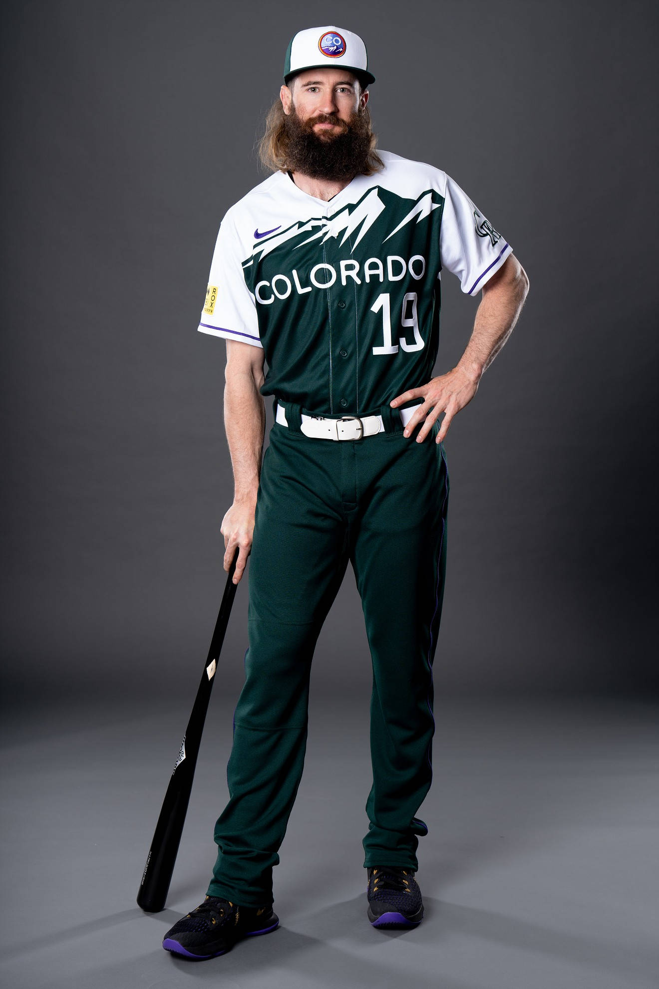 Colorado Rockies 桌布 壁紙 — 留鬍鬚的棒球選手穿著科羅拉多洛磯隊制服，在灰色攝影棚背景前自信地擺姿勢握著球棒。