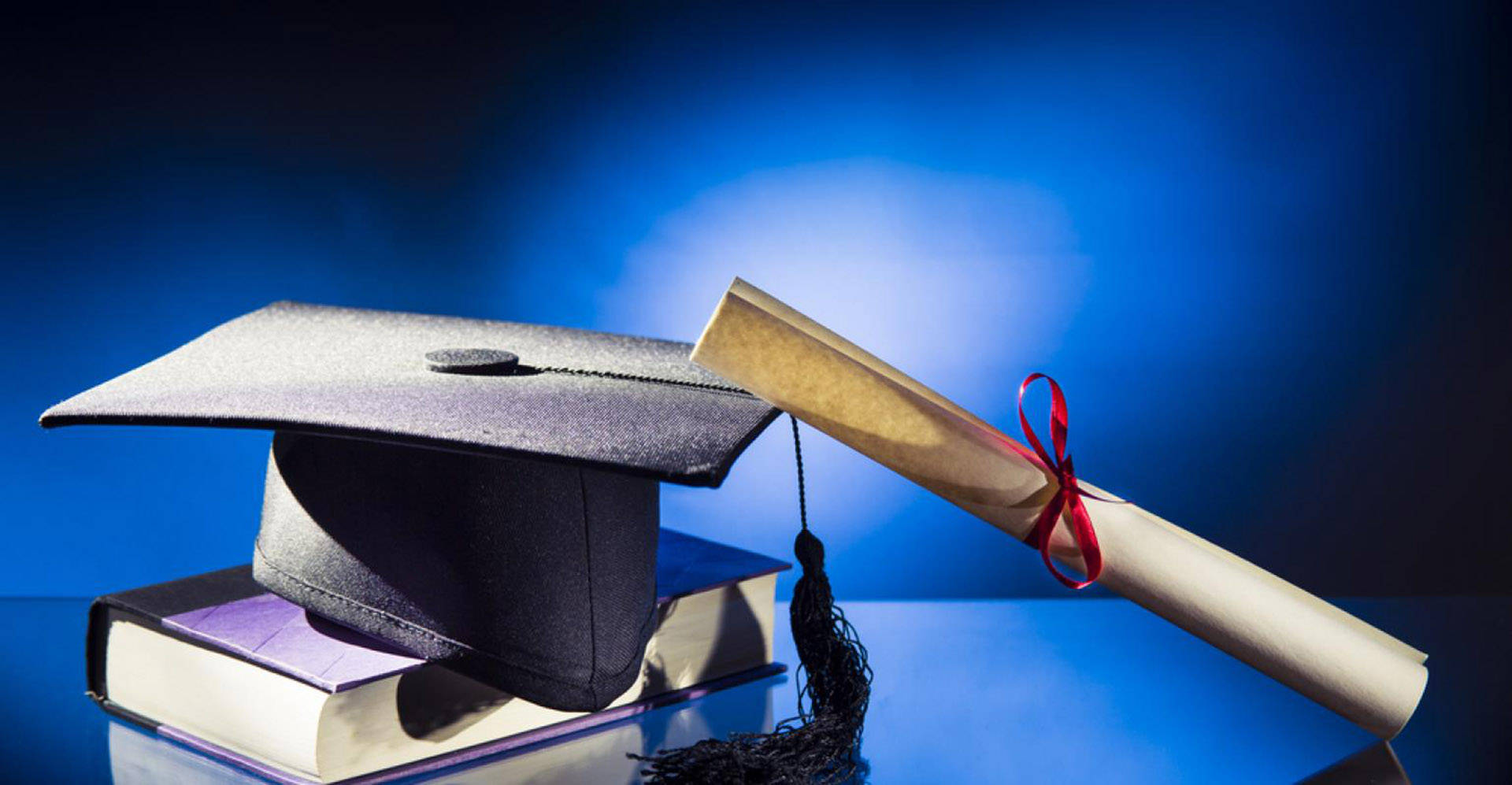 Graduation 桌布 壁紙 — 畢業帽和文憑卷軸放在堆疊的書本上，背景為深藍色漸變。