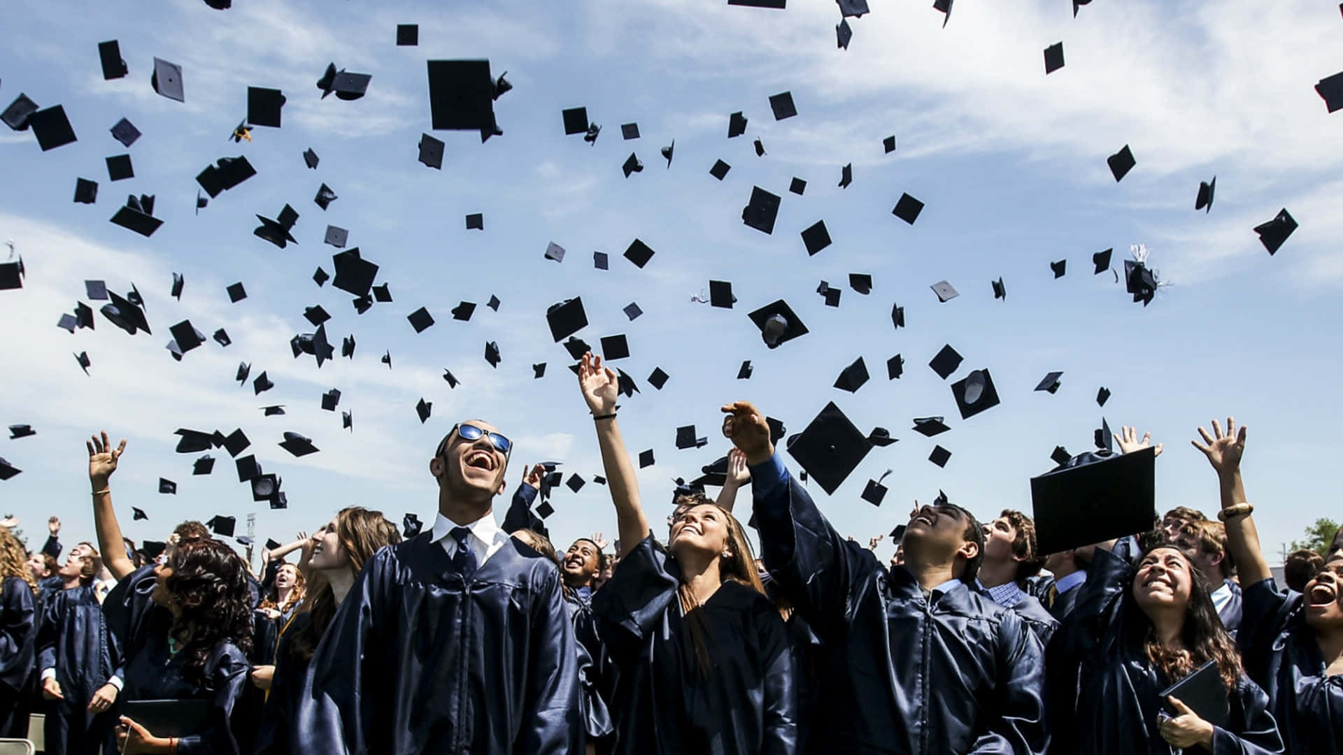 Graduation 桌布 壁紙 — 畢業生身穿深色畢業袍，在晴朗的日子裡歡快地將黑色學士帽拋向明亮的藍天。