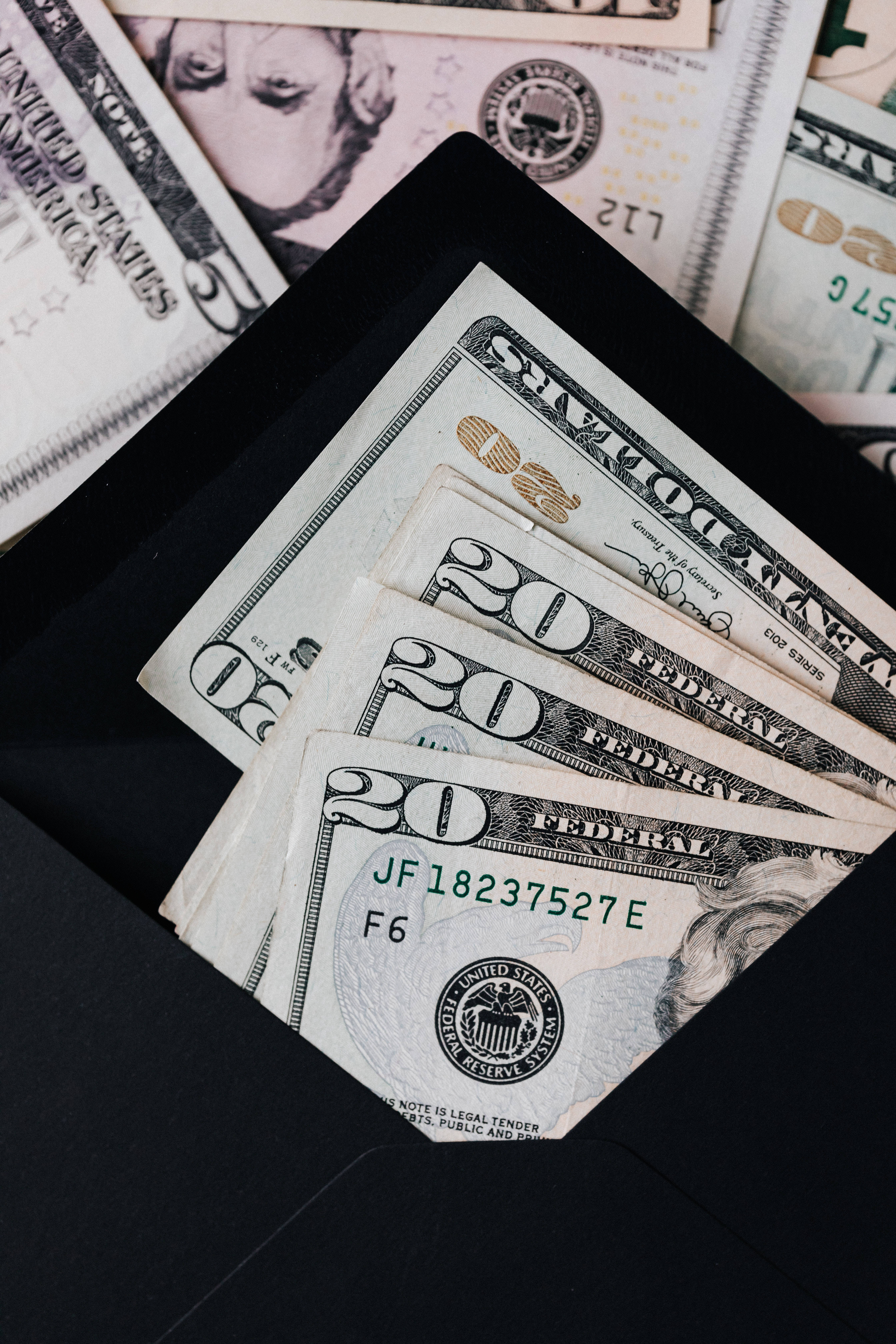 金錢 桌布 壁紙 — 疊起的二十美元鈔票從黑色信封中灑出，背景是更多的現金。