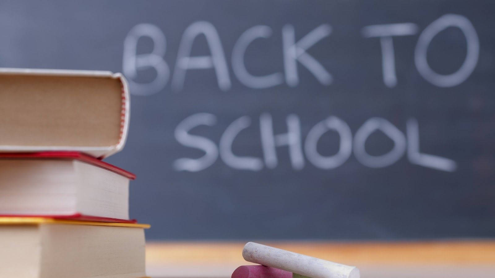 學校 桌布 壁紙 — 疊起的書本和粉筆放在一塊寫有「BACK TO SCHOOL」的黑板前，背景柔和。
