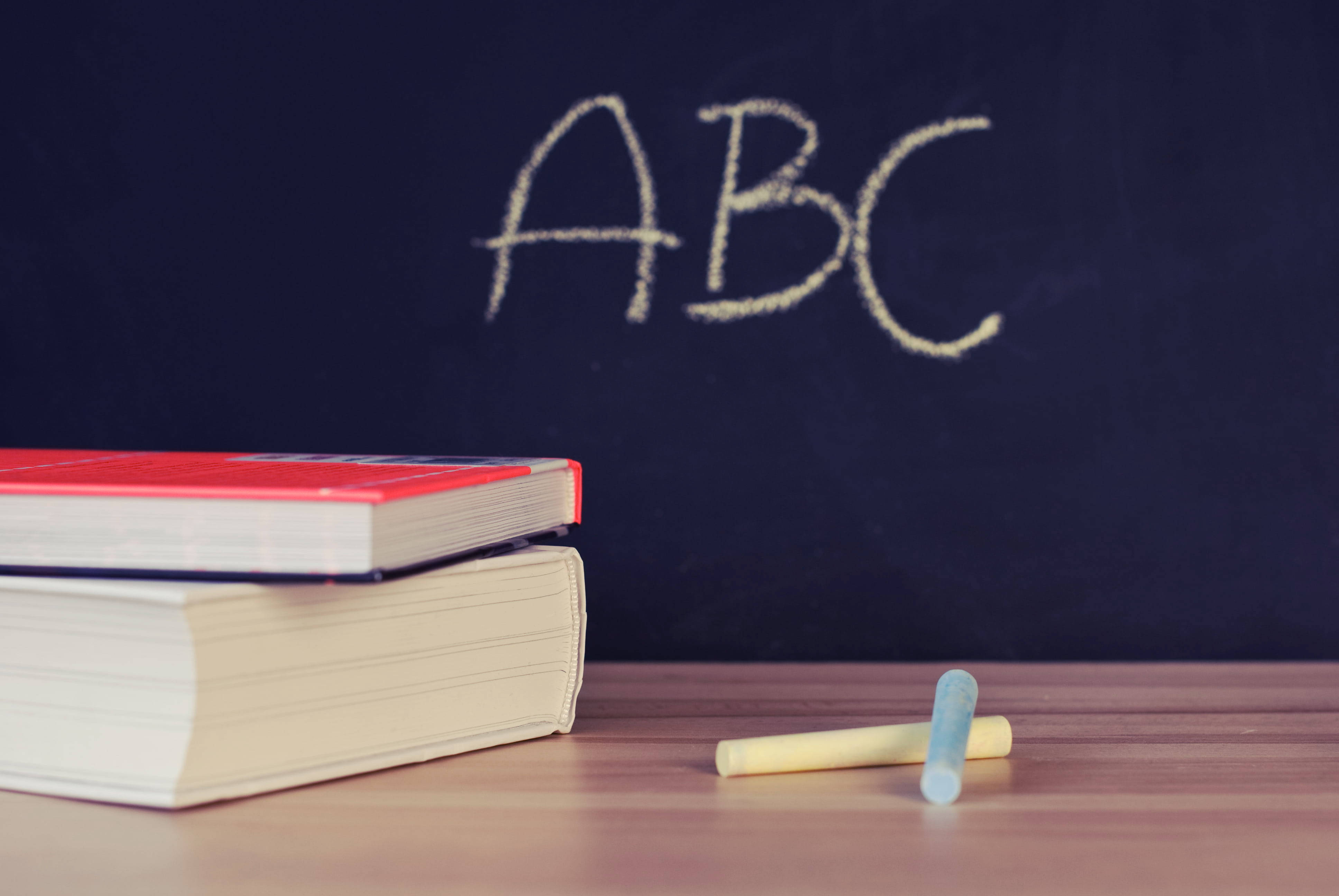 abc 桌布 壁紙 — 疊起的書本和粉筆放在木桌上，前面是黑板，上面用白色粉筆寫著ABC。