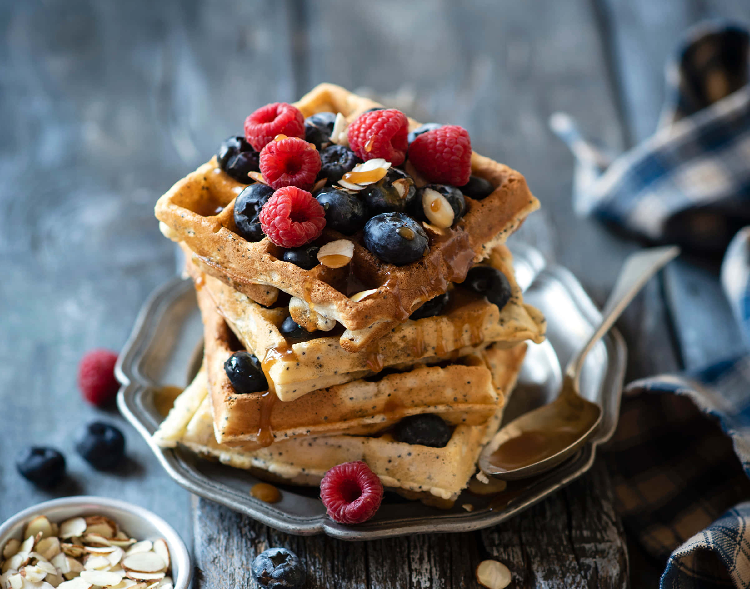 Waffle 桌布 壁紙 — 疊起的金黃色鬆餅，上面放上新鮮覆盆子、藍莓和杏仁片，淋上糖漿，放在鄉村風木桌上。