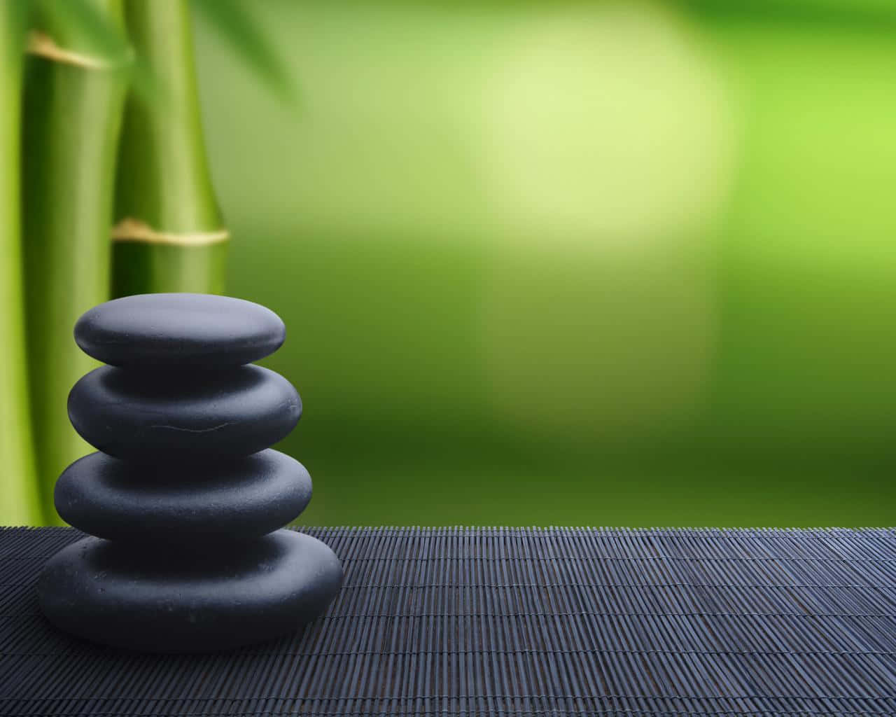 禪 桌布 壁紙 — 疊起的黑色禪石放在深色竹蓆上，背景是柔和的綠色模糊竹子。