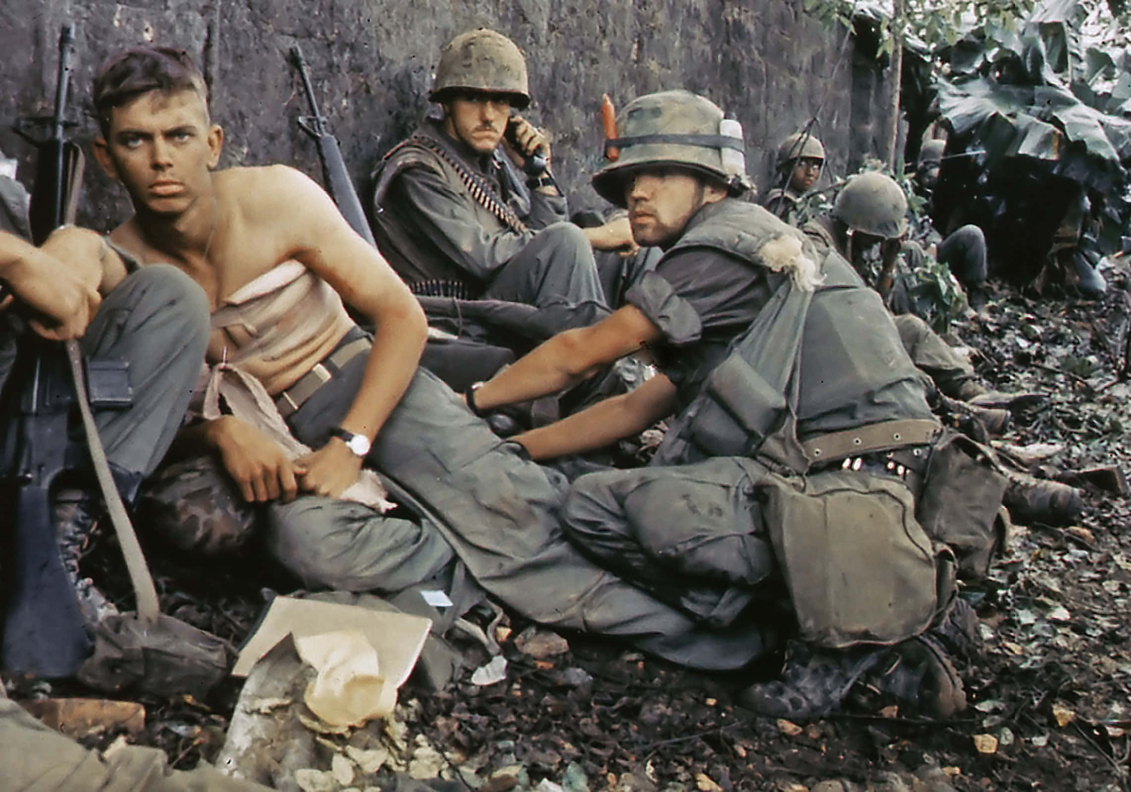 Vietnam War 桌布 壁紙 — 疲憊的士兵身穿叢林迷彩，靠著石牆休息，周圍有樹葉和散落的裝備。