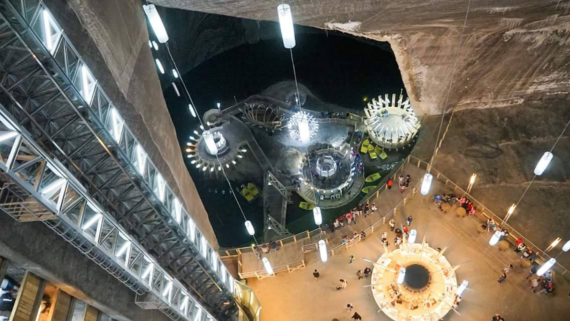 Romania 桌布 壁紙 — 發光地下洞穴轉變為未來展覽空間的鳥瞰圖，懸掛燈光與探索圓形平台的訪客。