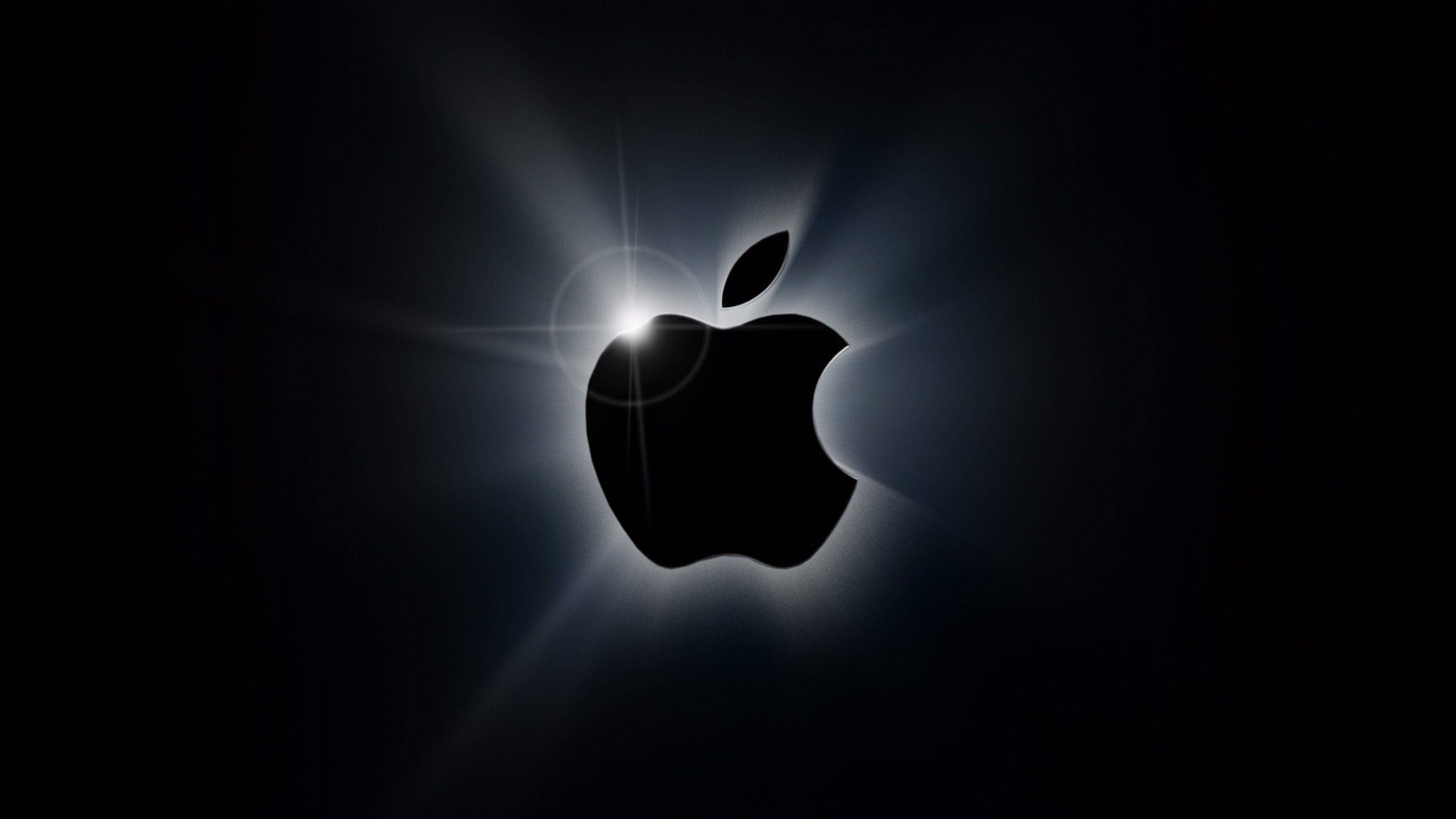 4K 桌布 壁紙 — 發光的Apple標誌剪影在深黑色背景上散發出明亮的光芒，並帶有鏡頭光暈效果。