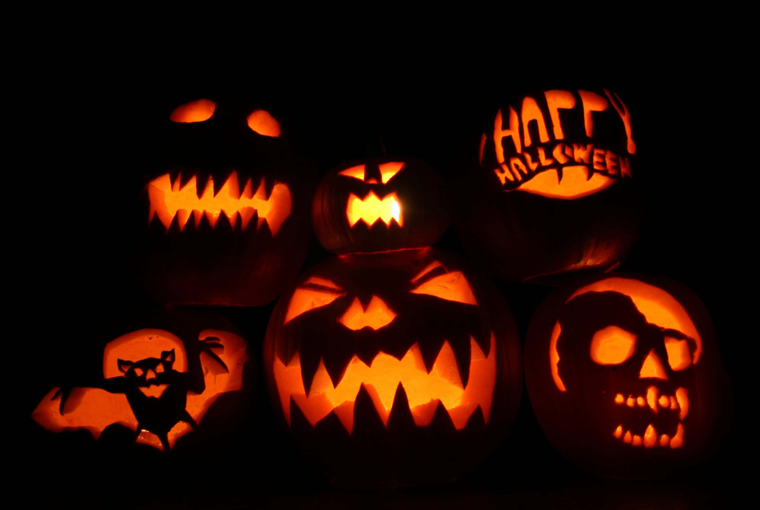 Pumpkin 桌布 壁紙 — 發光的傑克南瓜燈，帶有兇猛的雕刻面孔和「Happy Halloween」文字，照亮了黑暗的背景。