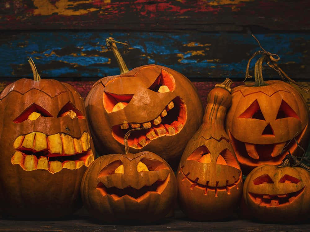 Jack O Lantern 桌布 壁紙 — 發光的傑克南瓜燈，帶有雕刻的笑容和鋸齒狀牙齒，放置在質樸的木質表面上，背景是風化的藍色牆壁。