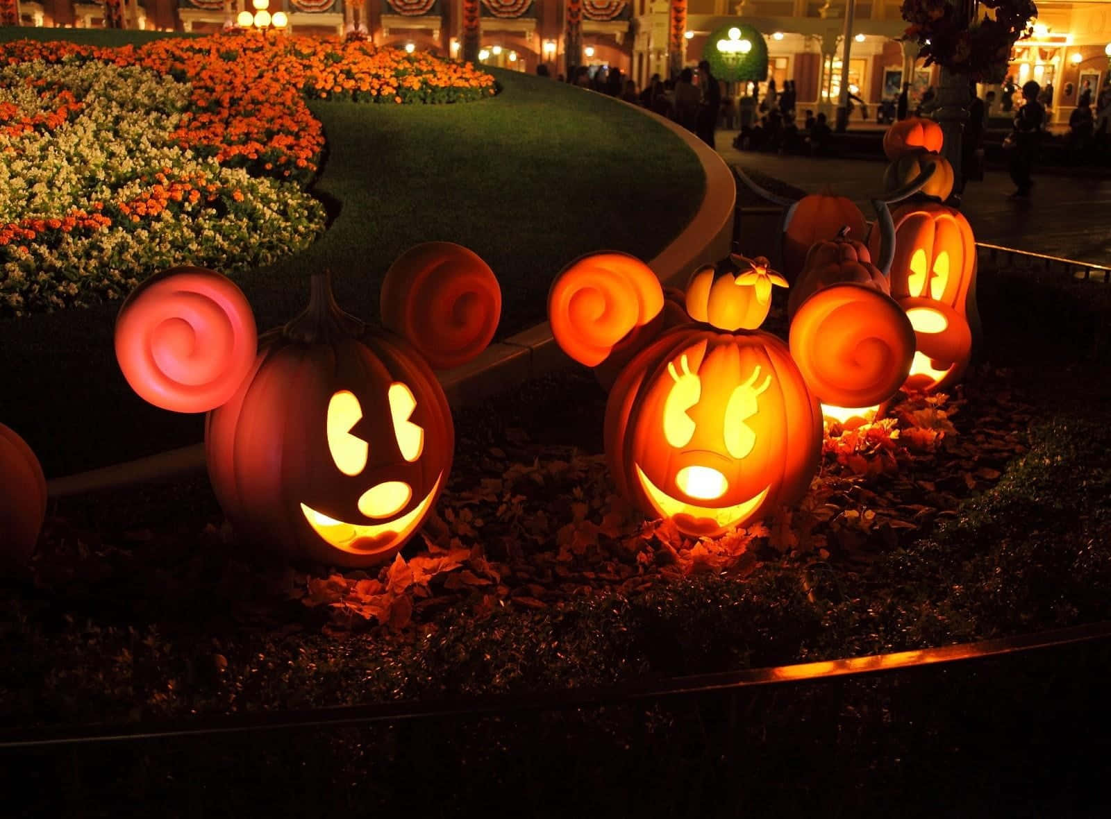 Disney Halloween 桌布 壁紙 — 發光的傑克南瓜燈，形狀像米奇和米妮老鼠，照亮了夜晚的花園，伴隨著秋葉和節日燈光。