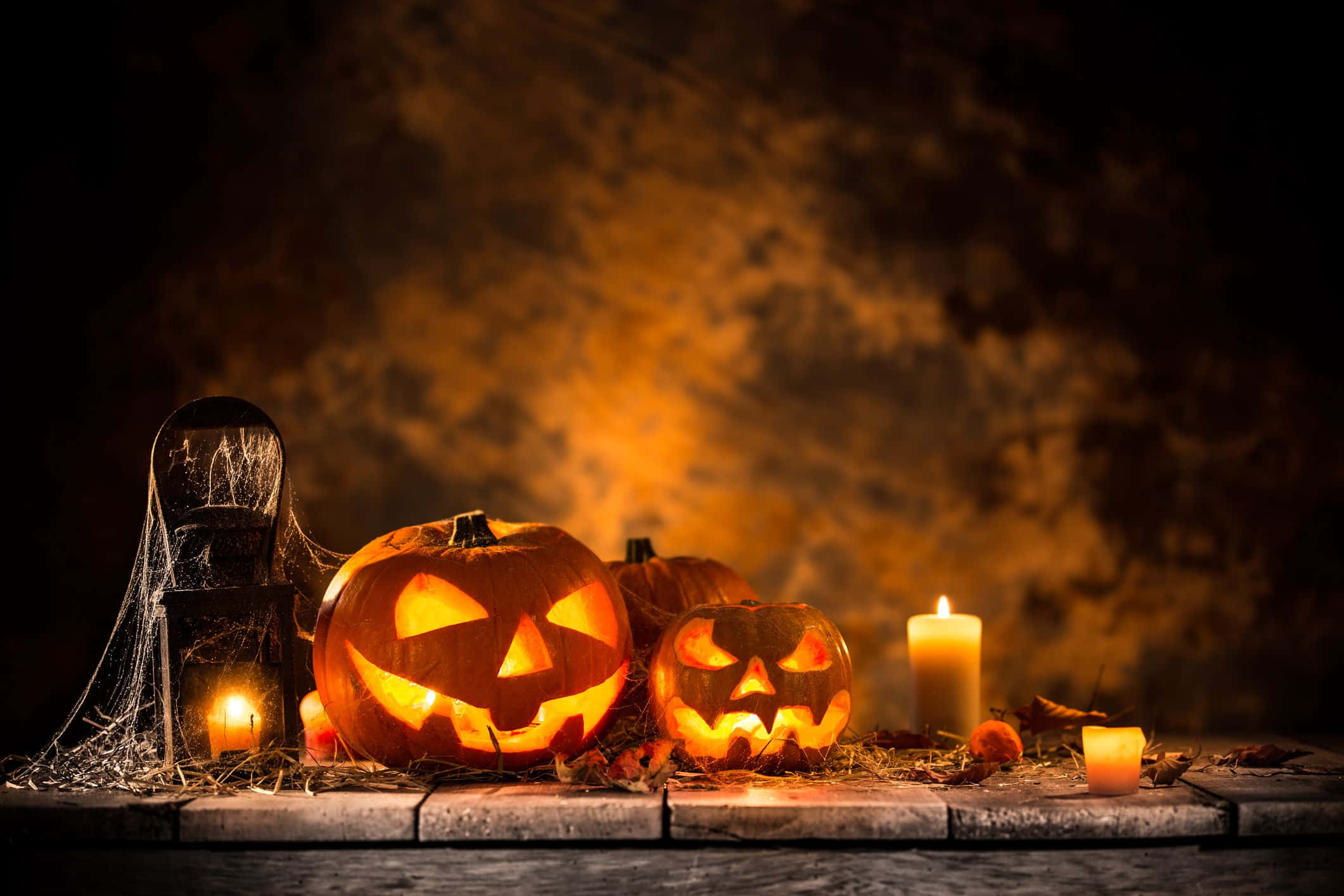 Spooky Halloween 桌布 壁紙 — 發光的傑克南瓜燈，燭光在佈滿蜘蛛網和秋葉的石頭表面上投射出詭異的陰影。