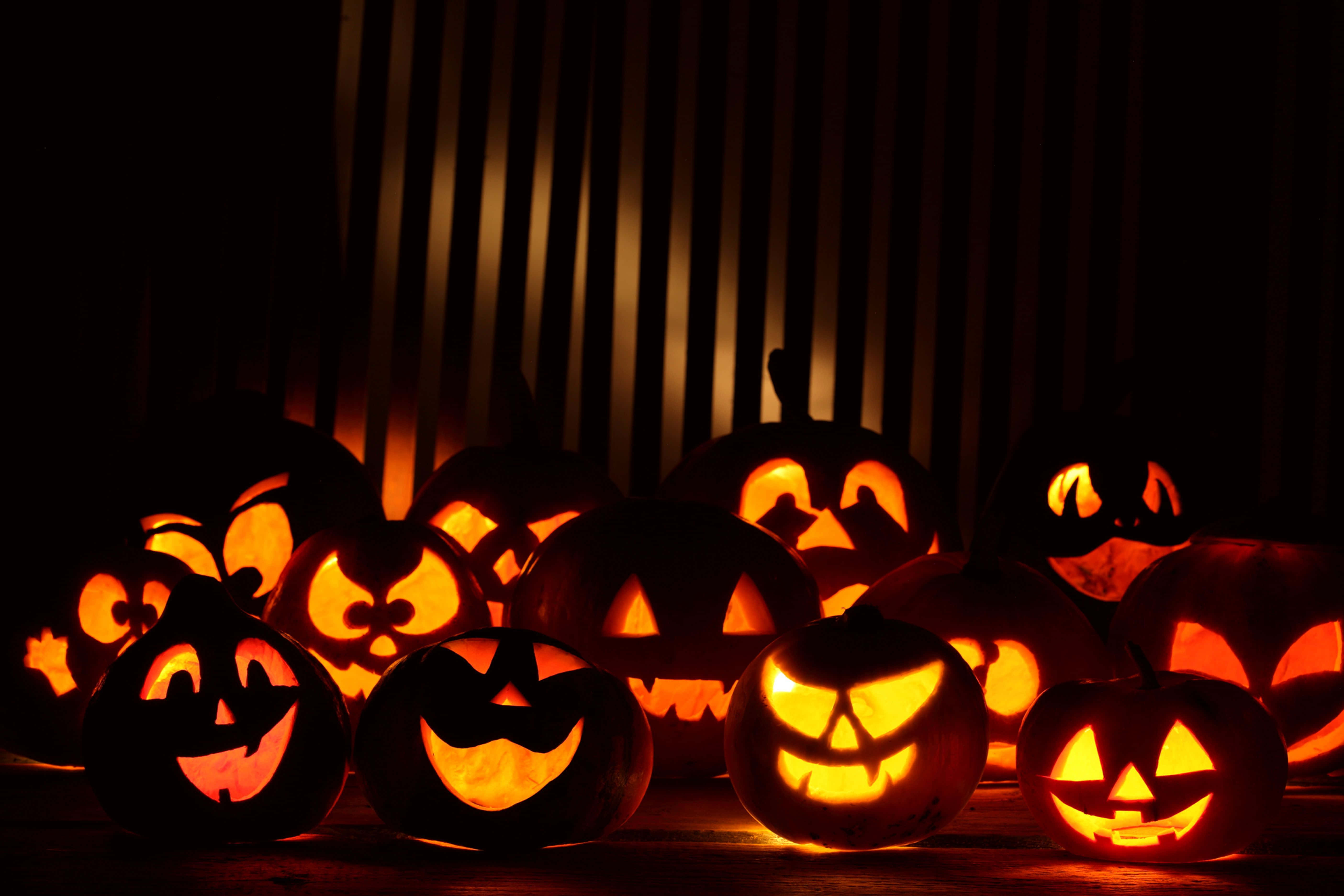 Jack O Lantern 桌布 壁紙 — 發光的傑克南瓜燈，雕刻著面孔，在條紋背景的襯托下照亮了黑暗的房間。