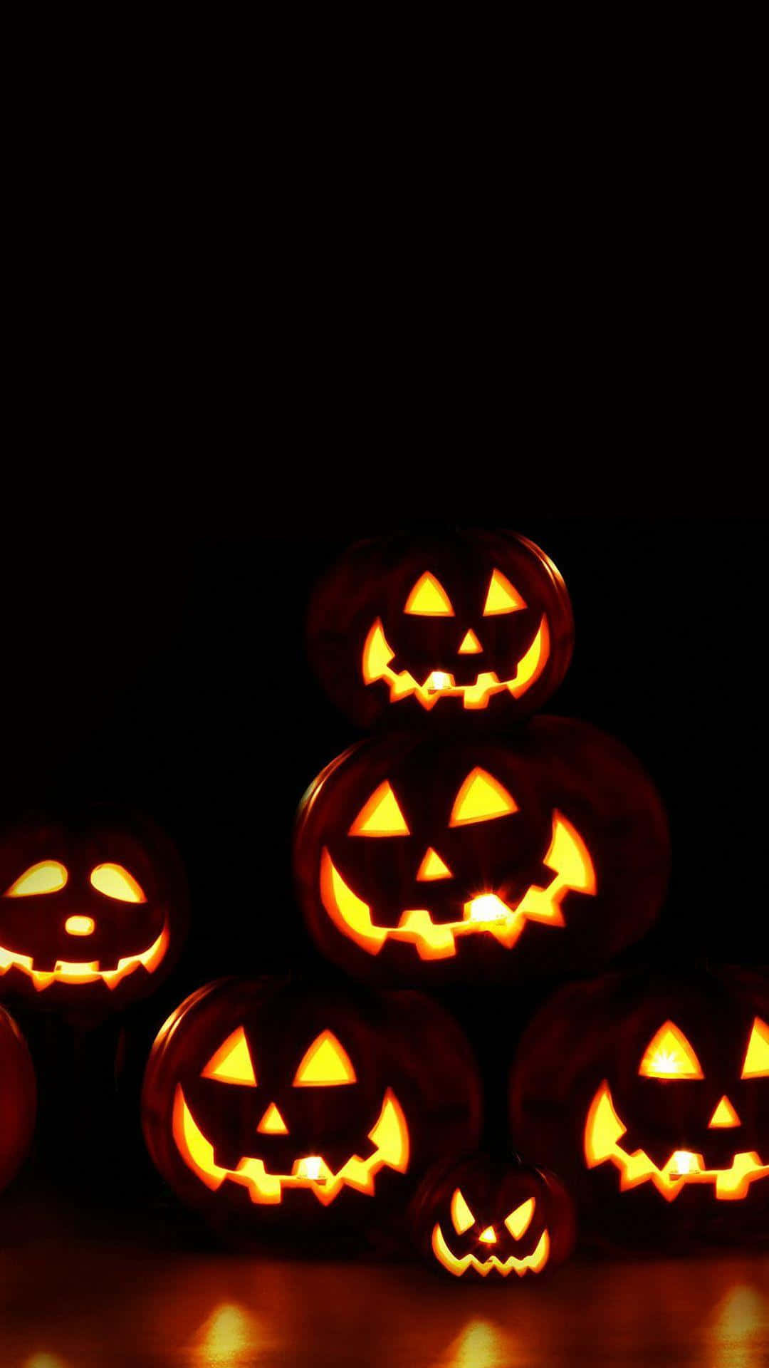 Spooky Halloween 桌布 壁紙 — 發光的傑克南瓜燈帶有雕刻的臉孔，在黑暗背景下散發出溫暖的光芒。