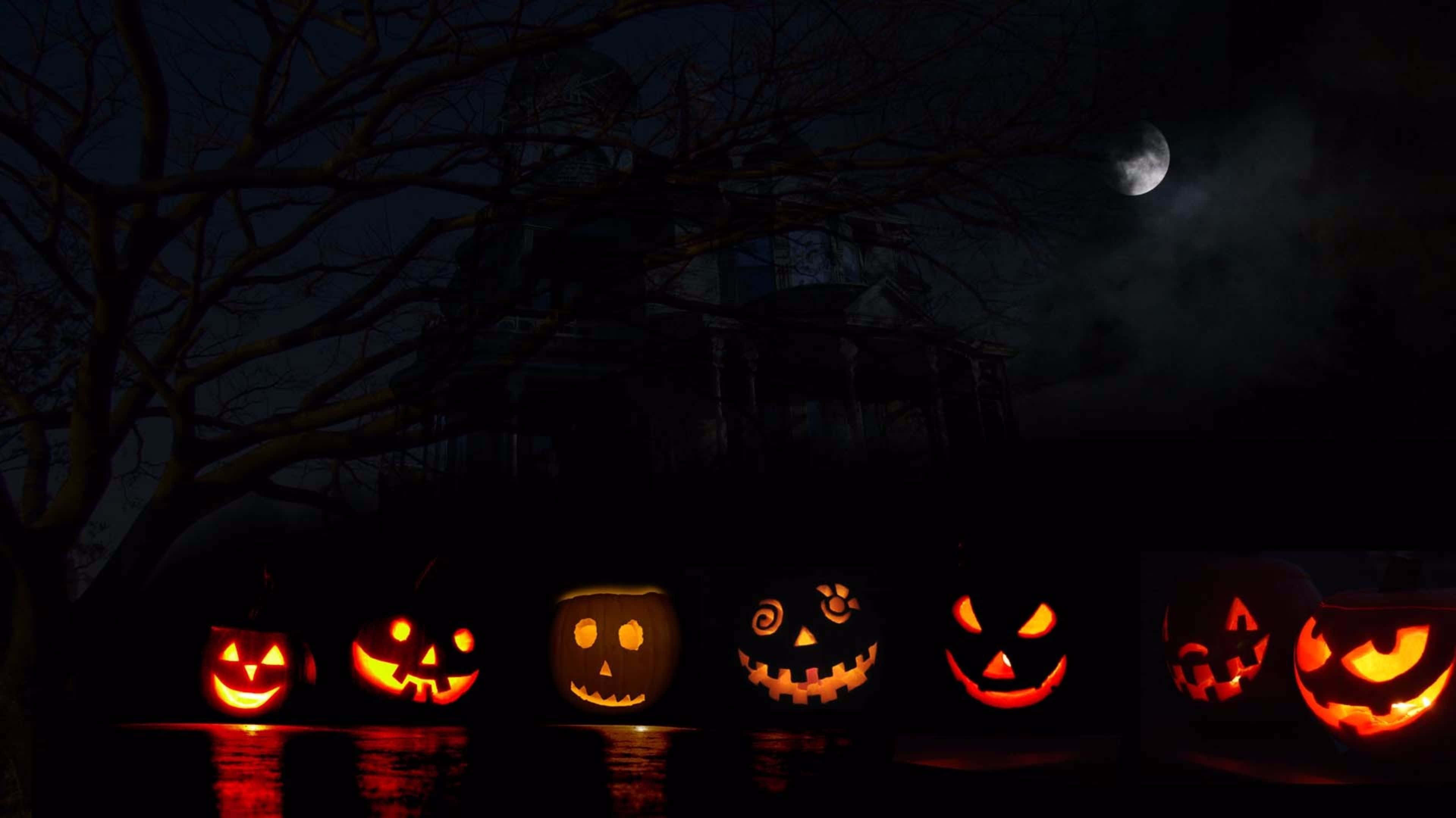 Neon Halloween 桌布 壁紙 — 發光的傑克南瓜燈排列在一條黑暗的小路上，背景是月光下的天空、光禿禿的樹木和一棟陰森的房子。