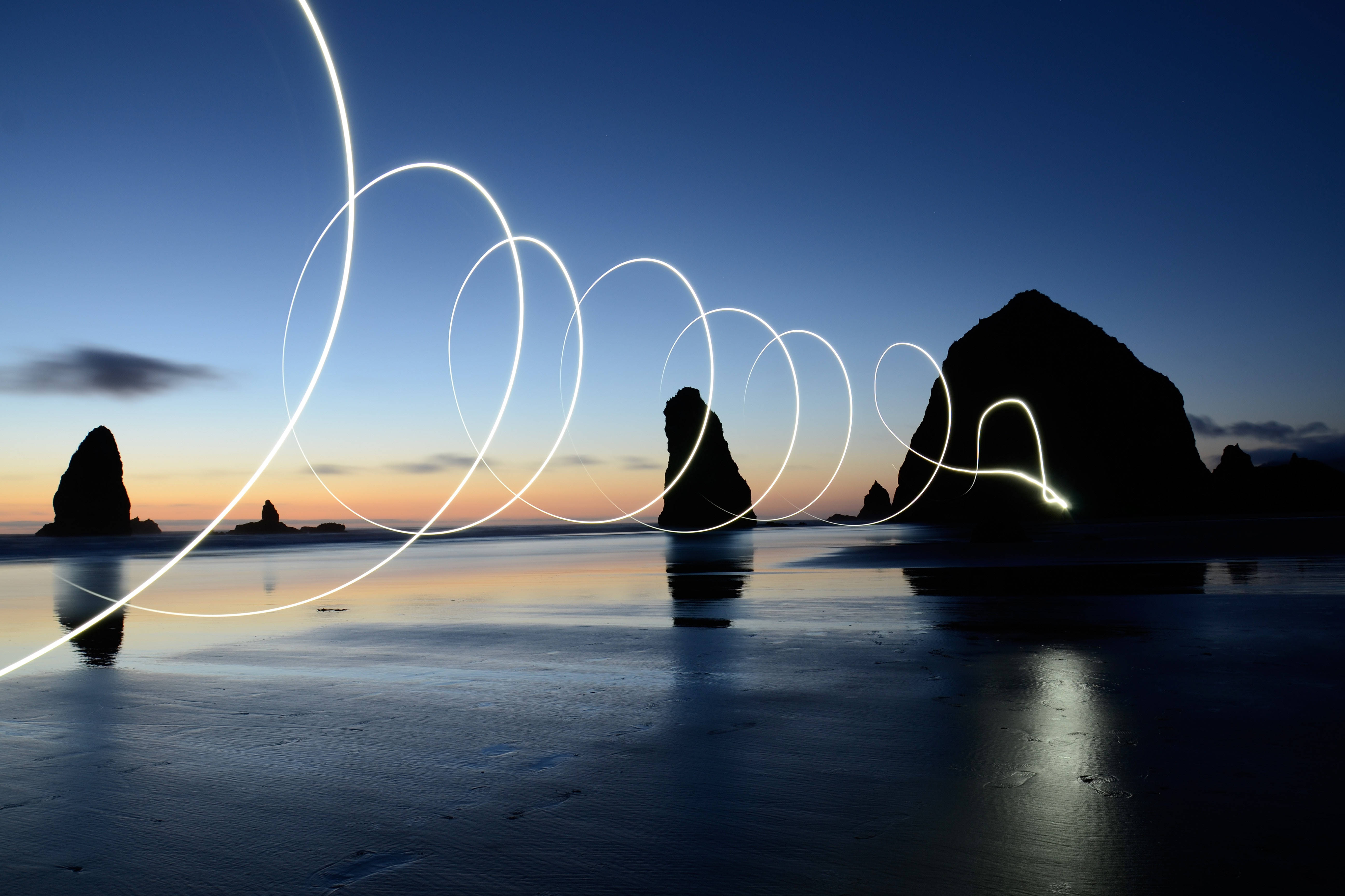 Tumblr Sunset Desktop 桌布 壁紙 — 發光的光跡在黃昏時分平靜的海灘上旋轉，剪影般的海蝕柱在平靜的水面上倒映。