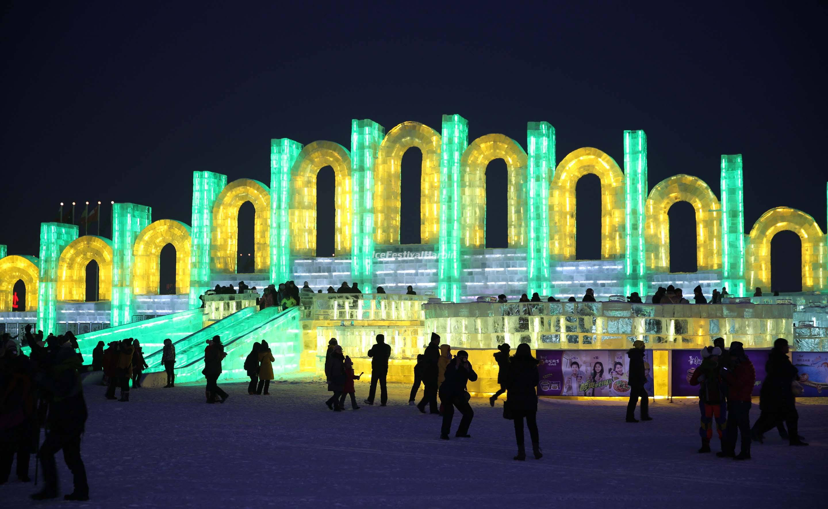 Harbin 桌布 壁紙 — 發光的冰拱門在漆黑的夜空下閃爍著綠色和黃色的光芒，雪地上的人影在漫步。