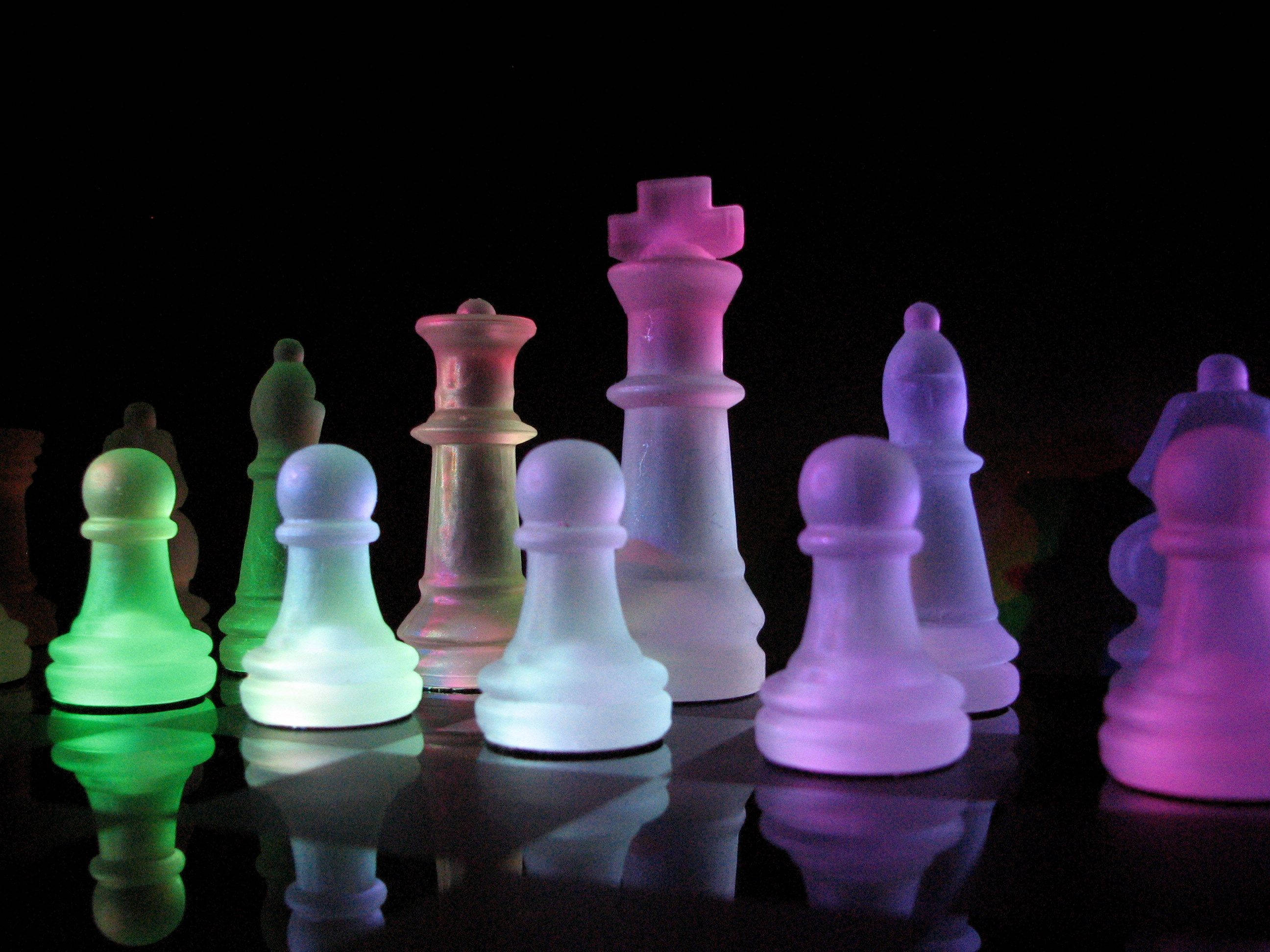 西洋棋 桌布 壁紙 — 發光的半透明國際象棋棋子以鮮豔的霓虹色調立在黑色背景的反射表面上。