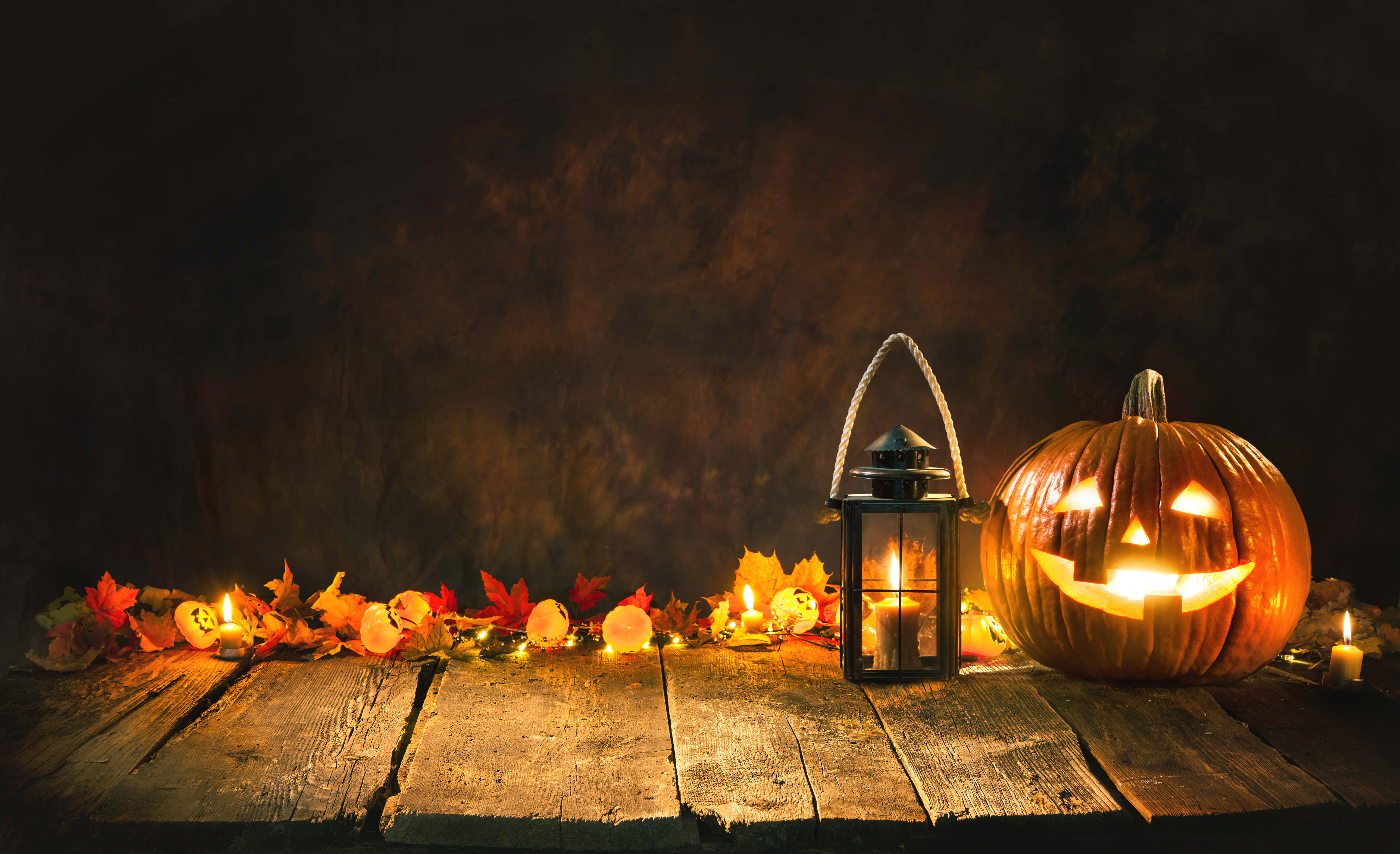 Minimalist Halloween 桌布 壁紙 — 發光的南瓜燈和燈籠在質樸的木桌上為秋葉和蠟燭投下溫暖的光芒。
