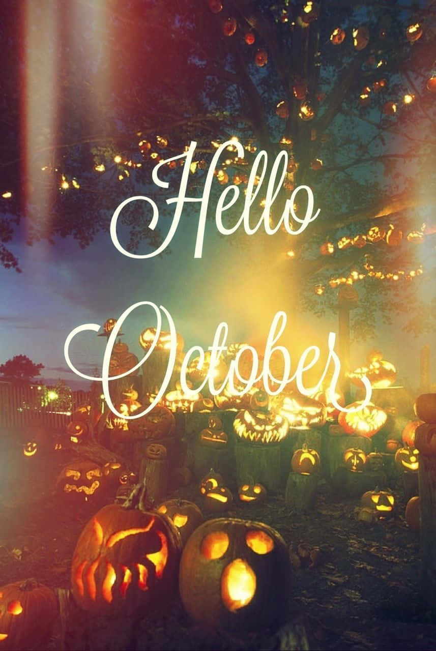 Hello October With Pumpkin 桌布 壁紙 — 發光的南瓜燈照亮了節日般的秋夜，樹下裝飾著燈串和草書文字 Hello October。