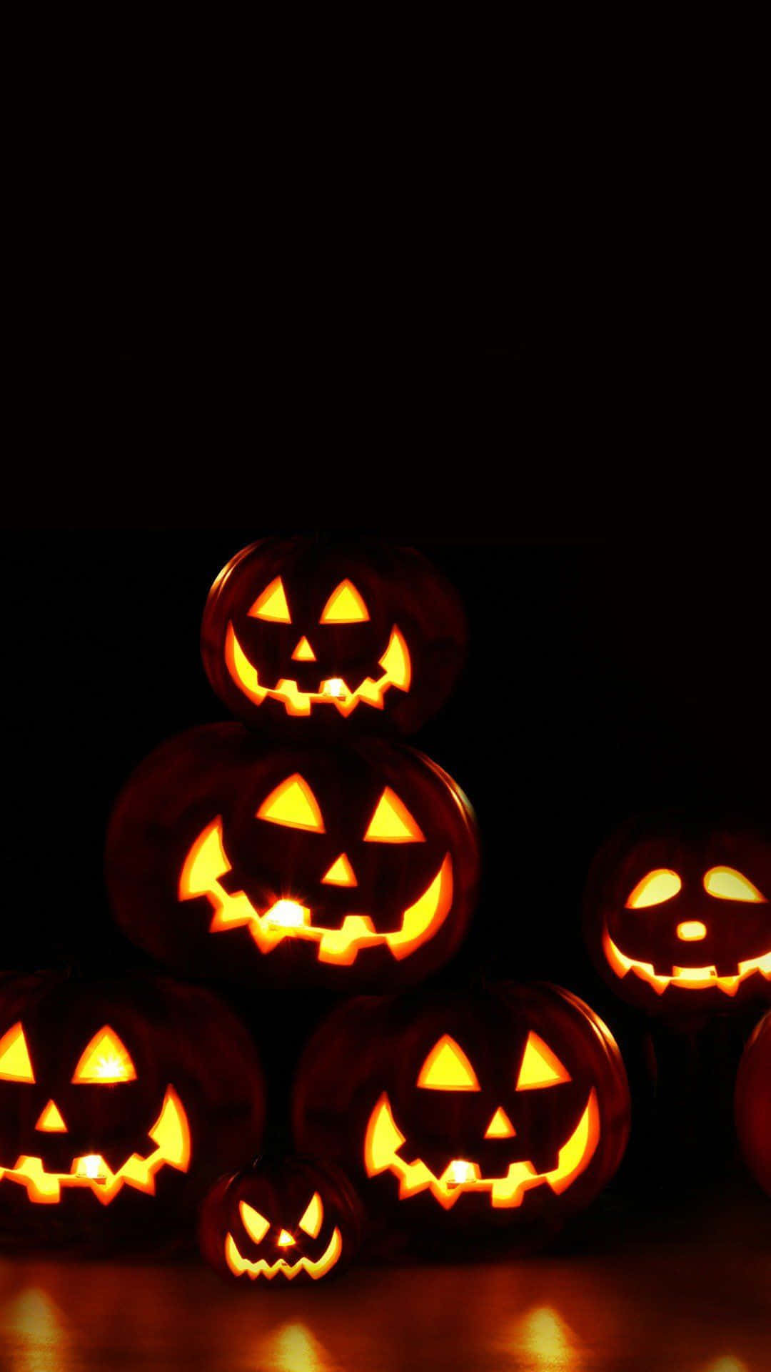 iPhone Halloween 桌布 壁紙 — 發光的南瓜燈籠，帶有雕刻的臉孔，堆疊並散落在黑暗背景上。