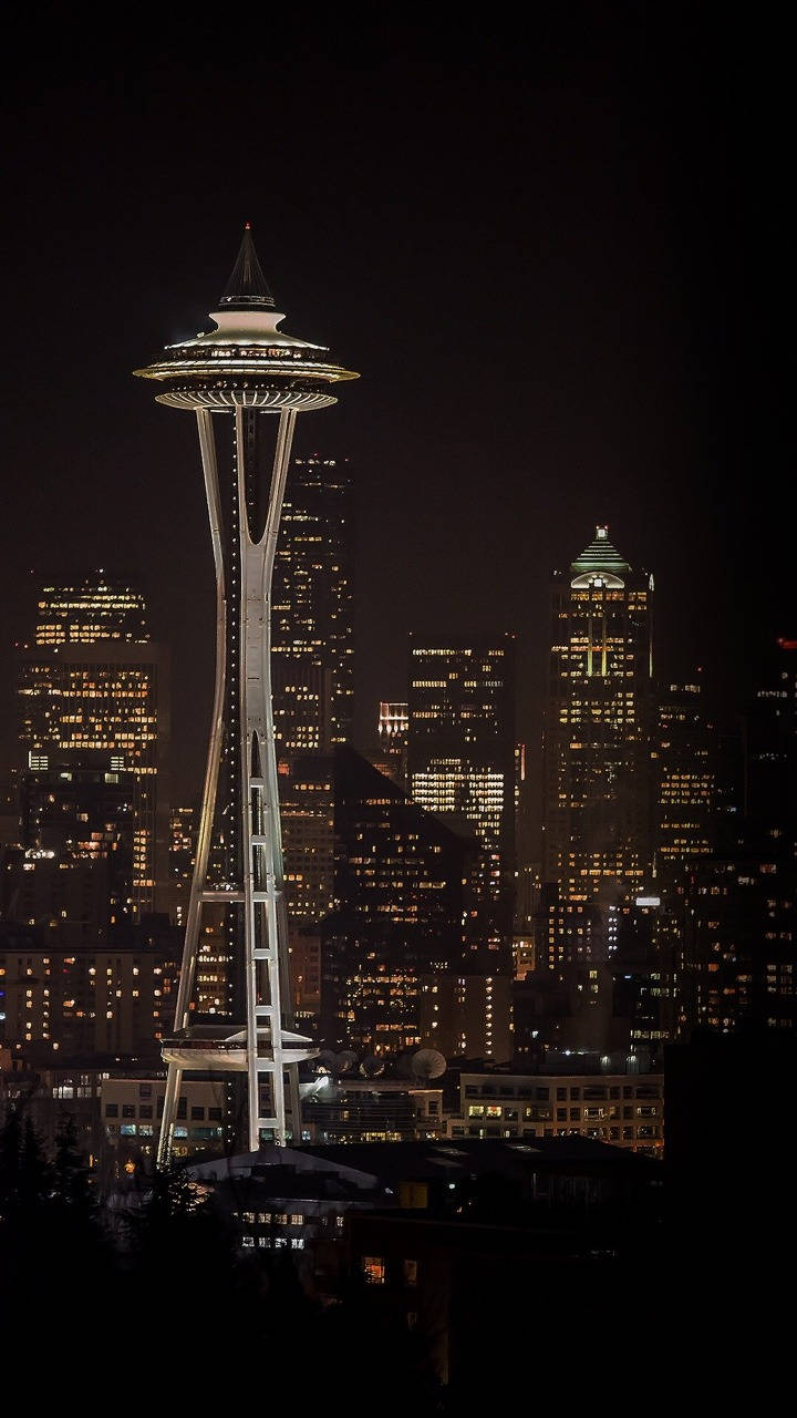 Washington 桌布 壁紙 — 發光的太空針塔在黑暗的天空下高高聳立，周圍是西雅圖充滿活力的夜景中閃爍的摩天大樓。