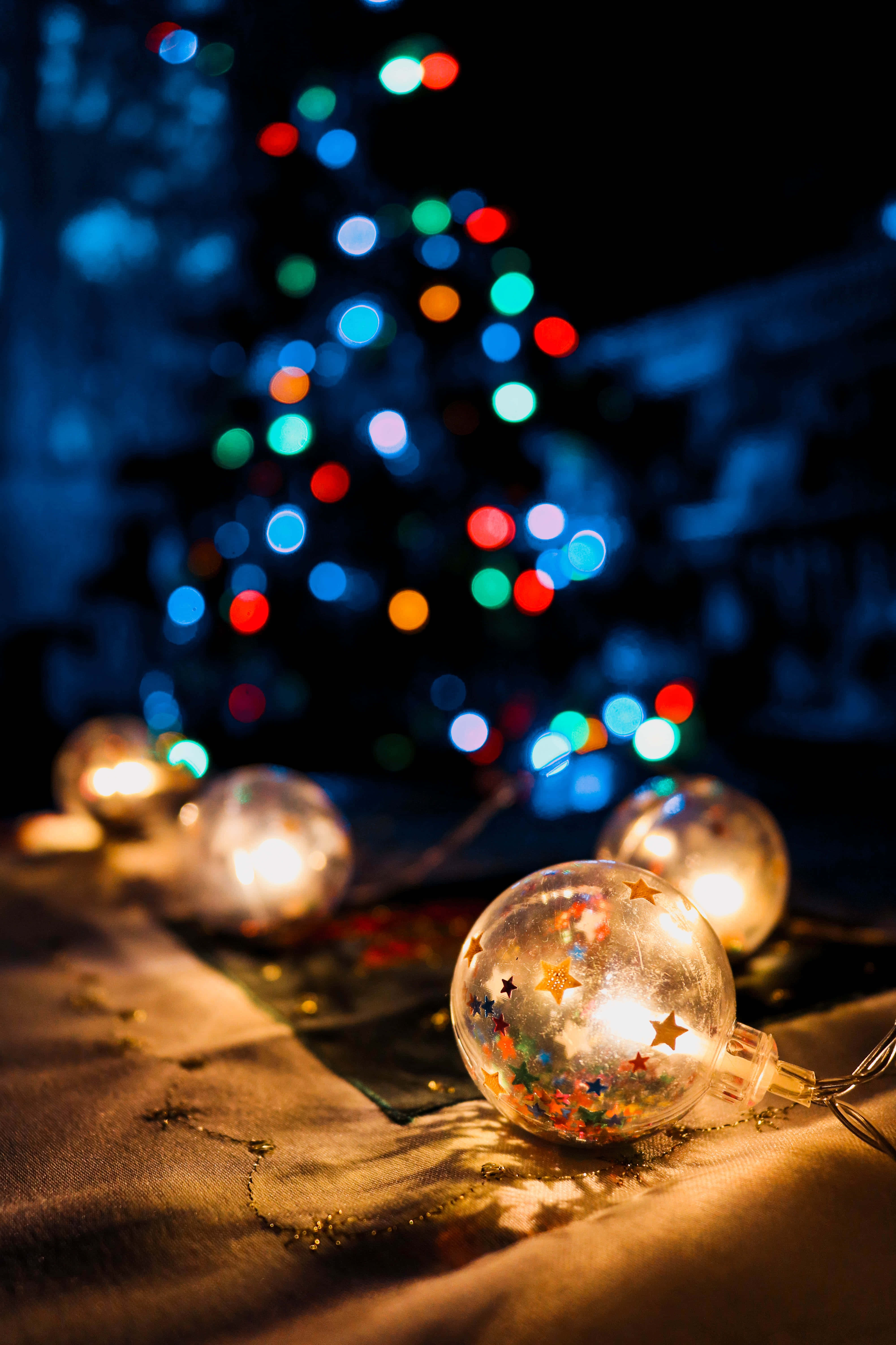 Christmas Light 桌布 壁紙 — 發光的星星裝飾品放置在帶有紋理的表面上，背景是散景聖誕樹。