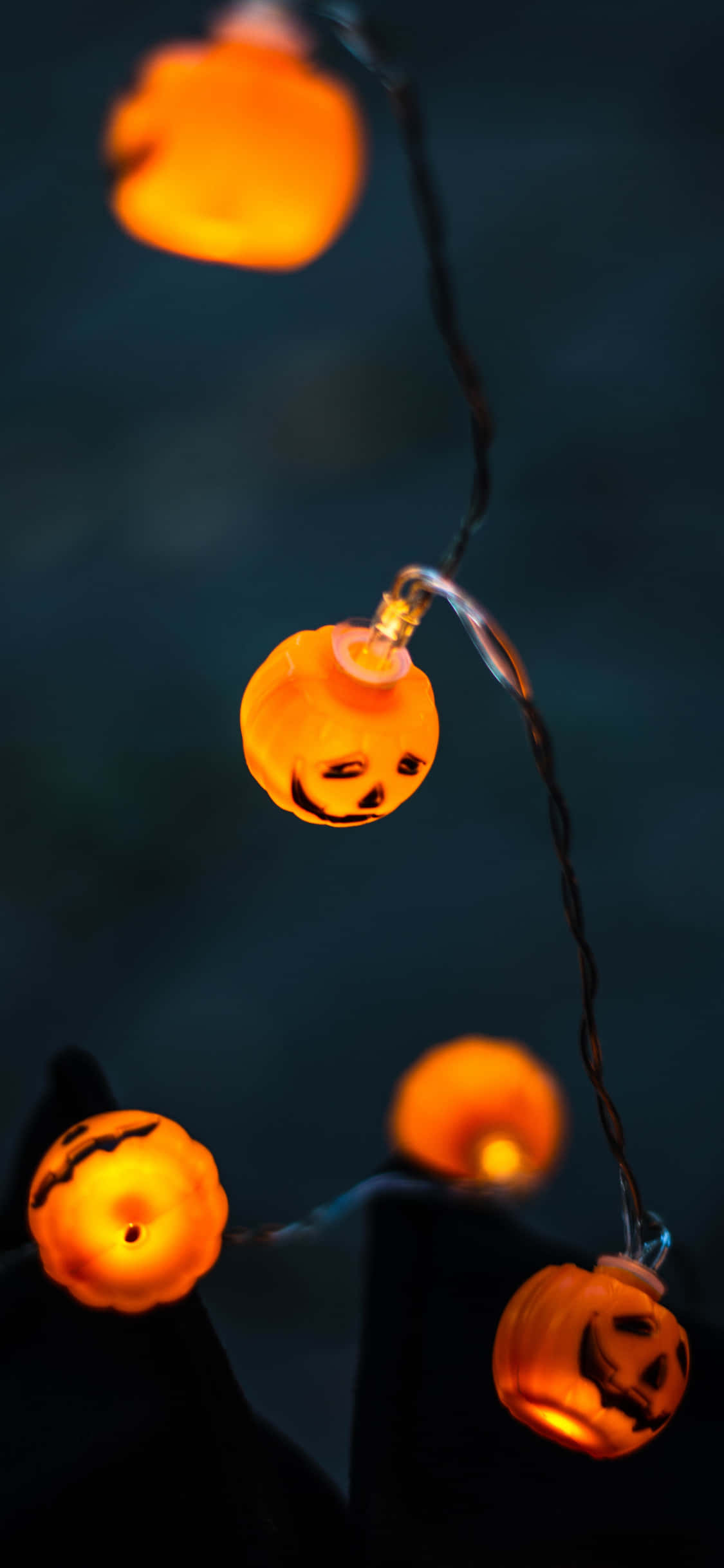 Jack O Lantern 桌布 壁紙 — 發光的橙色南瓜形燈泡掛在一條線上，背景為深藍色，營造出節日萬聖節氛圍。
