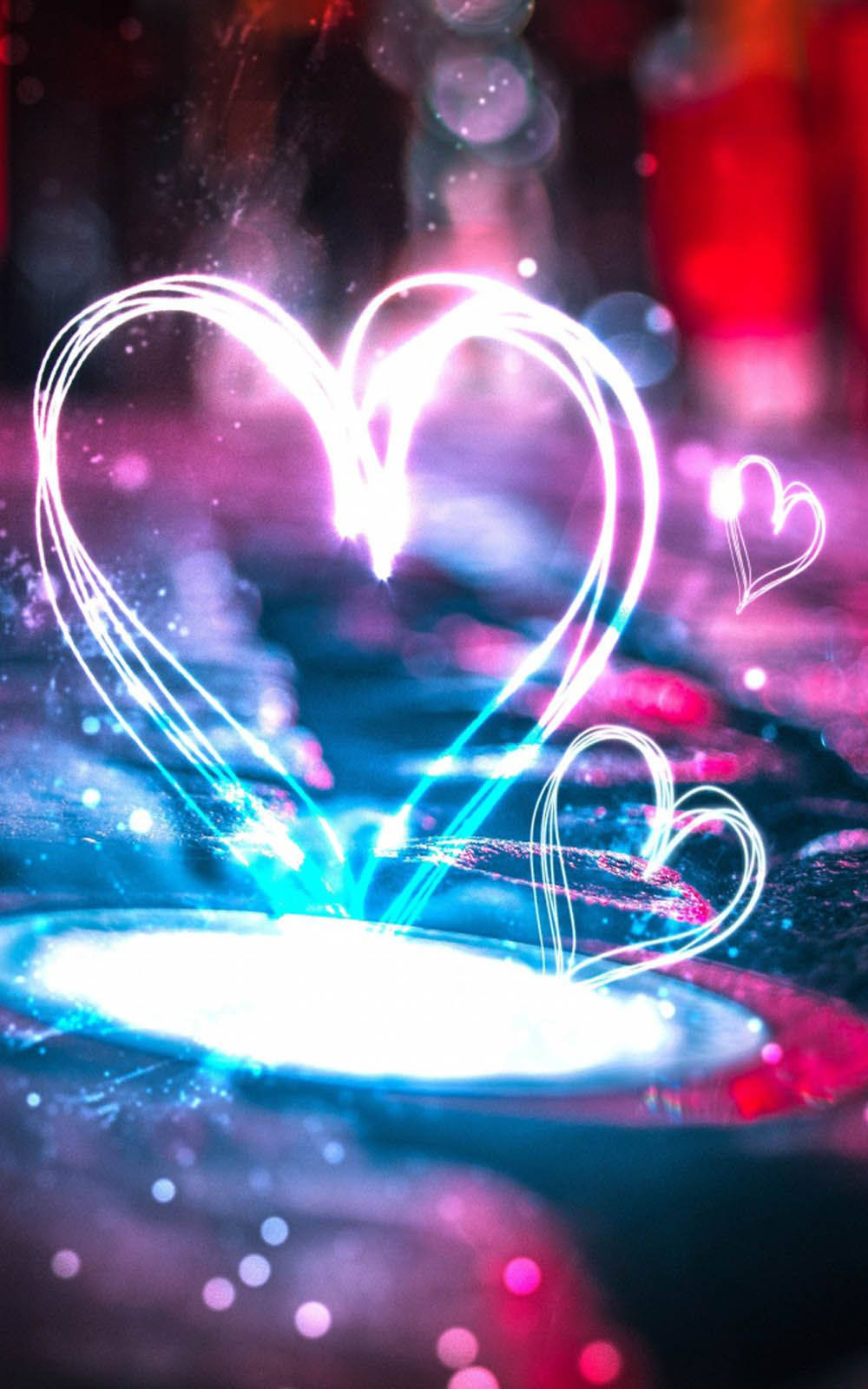 Love Heart 桌布 壁紙 — 發光的燈光軌跡在充滿活力的散景背景上形成交織的心形，並帶有閃爍的粒子。