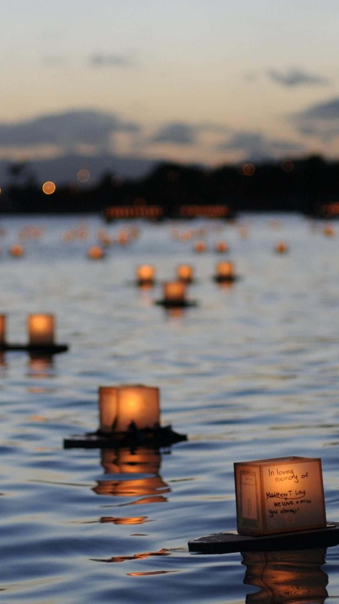 Funeral 桌布 壁紙 — 發光的燈籠在黃昏時平靜地漂浮在平靜的水面上，遠山在柔和的暮色天空下形成剪影。