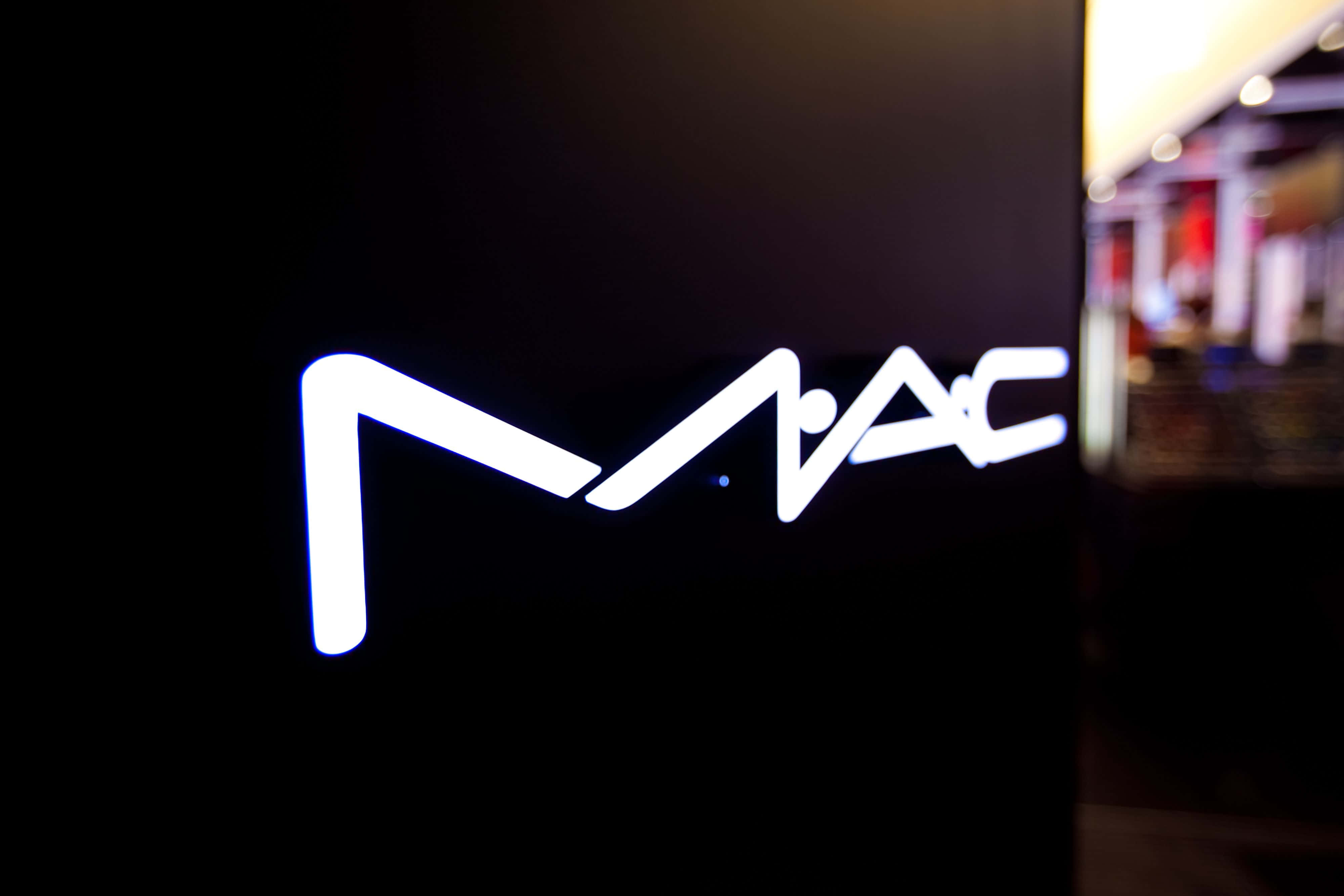 Mac Cosmetics 桌布 壁紙 — 發光的白色MAC標誌招牌在黑暗的牆壁和模糊的室內背景中脫穎而出。