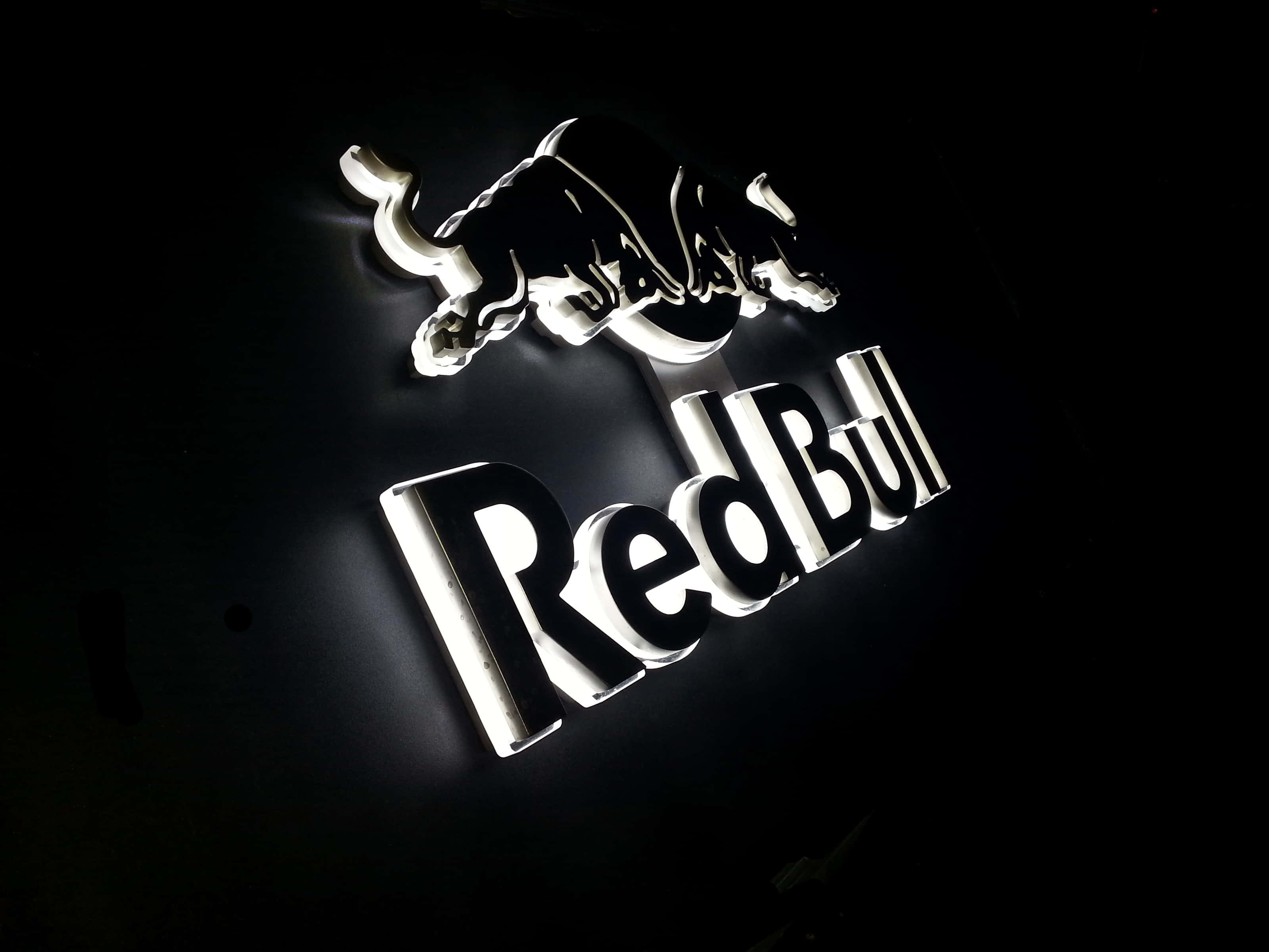 紅牛 桌布 壁紙 — 發光的白色Red Bull標誌，帶有跳躍的公牛圖案，在黑暗背景上照亮。