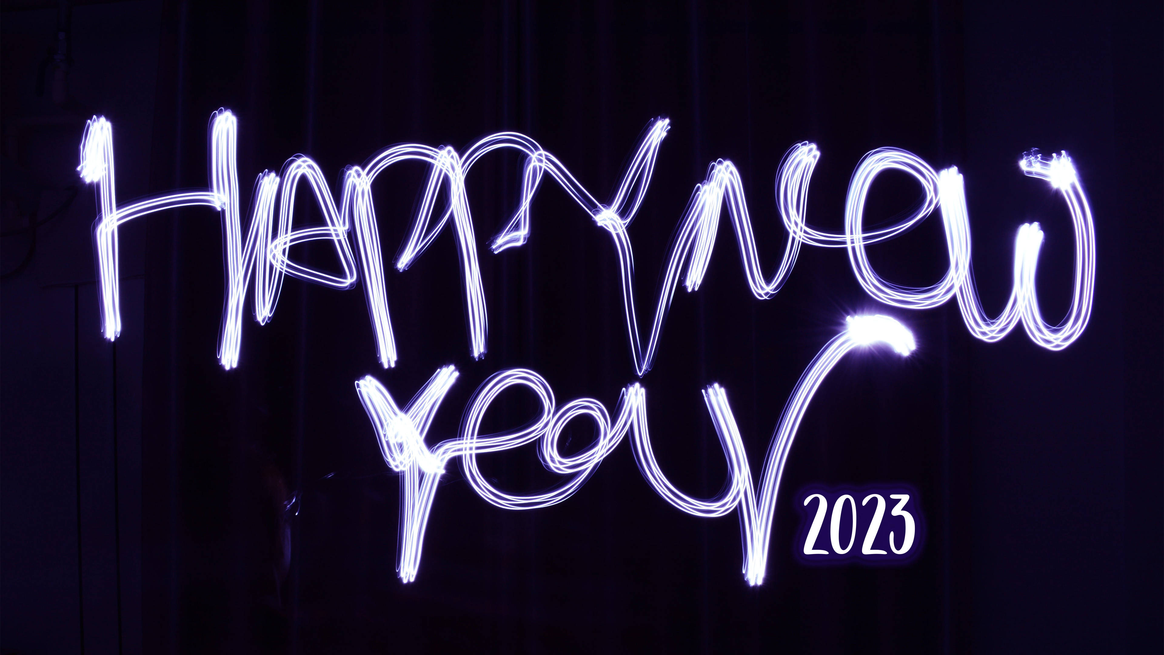 新年快樂 桌布 壁紙 — 發光的白色燈光繪製的「Happy New Year 2023」字樣在深色窗簾背景下閃耀。