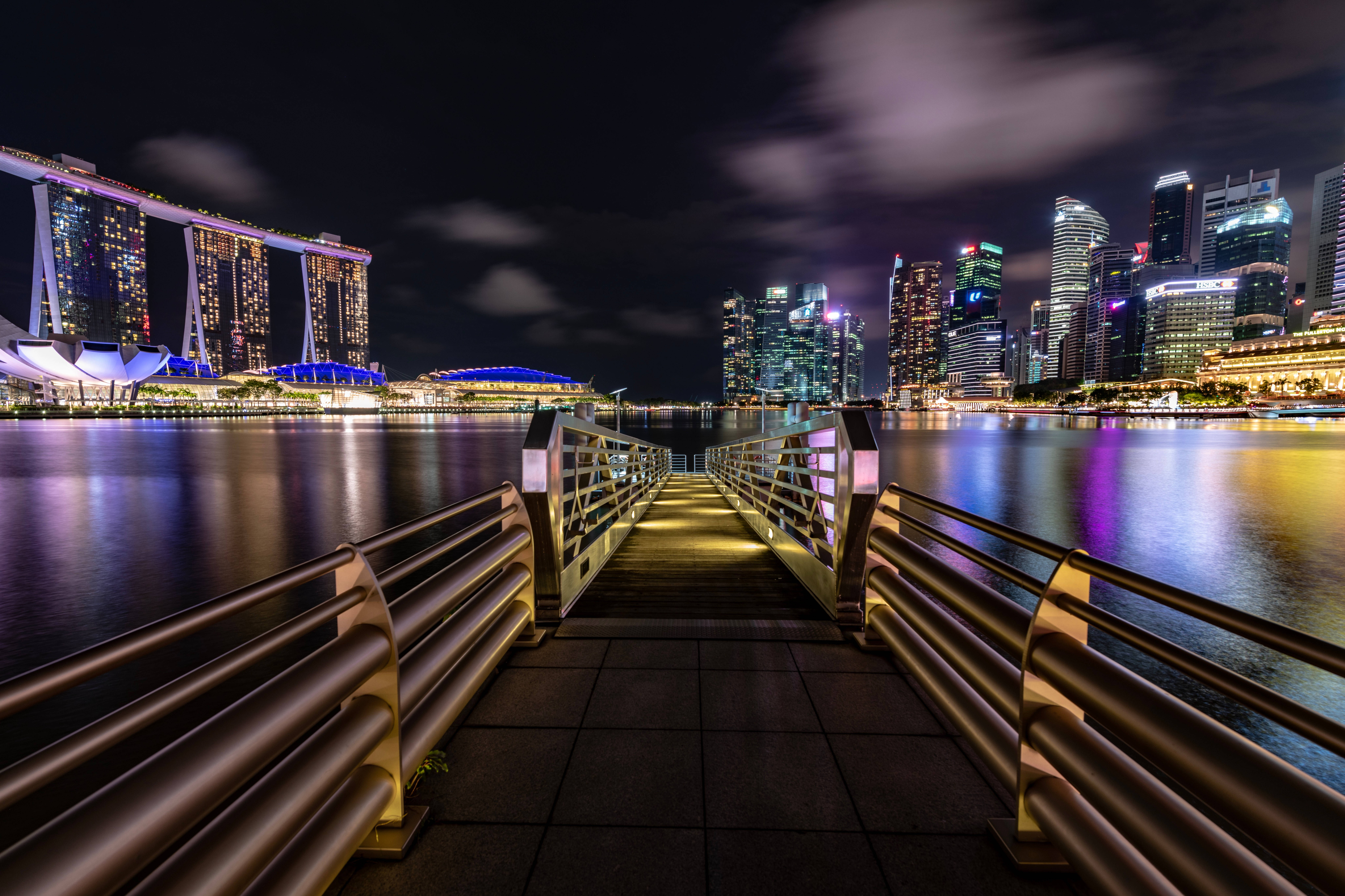 夜晚 桌布 壁紙 — 發光的碼頭通往新加坡耀眼的夜景，濱海灣金沙和摩天大樓倒映在平靜的水面上。