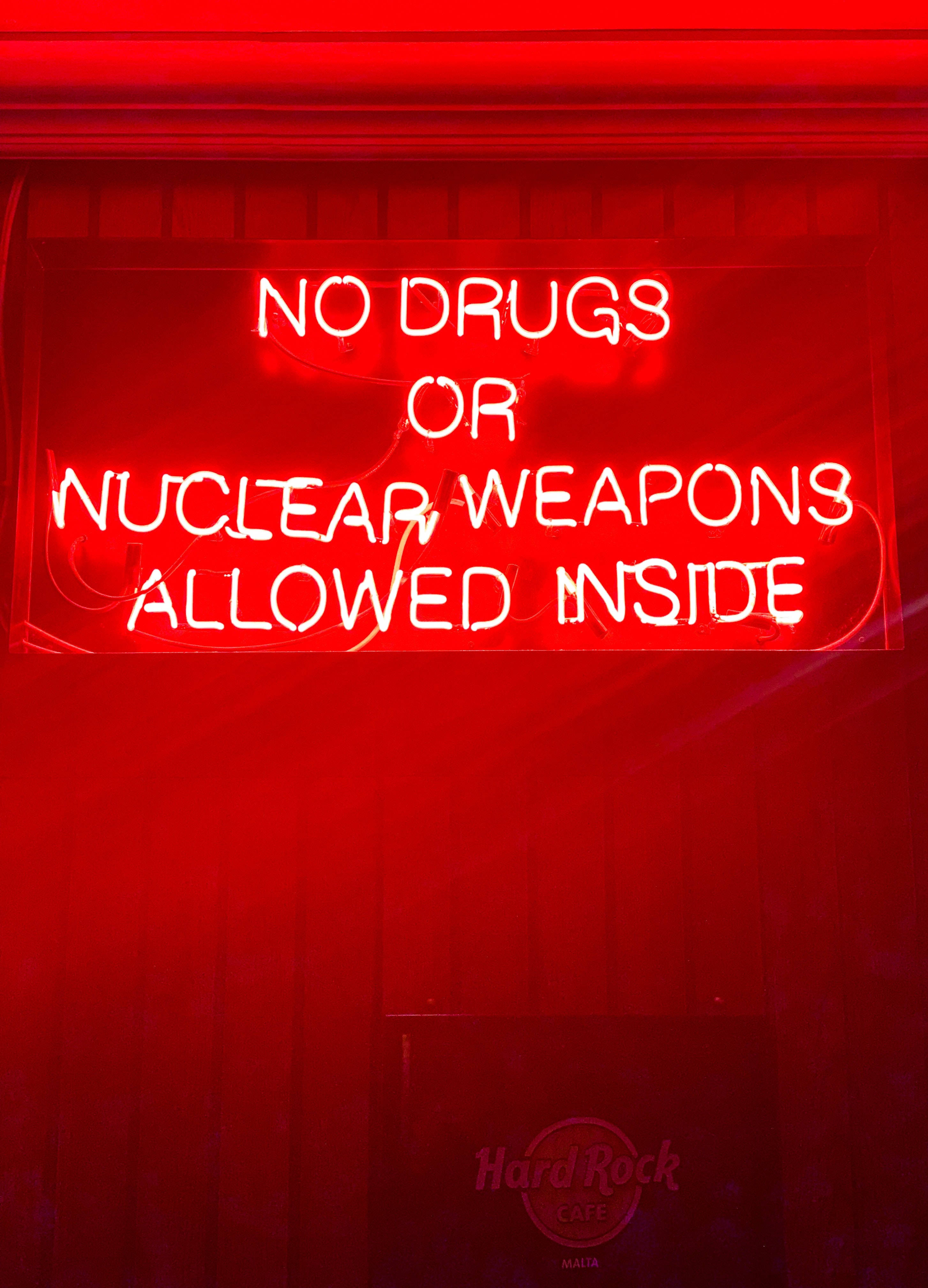 neon sign 桌布 壁紙 — 發光的紅色霓虹燈牌寫著禁止攜帶毒品或核武器進入，背景是深色木牆。