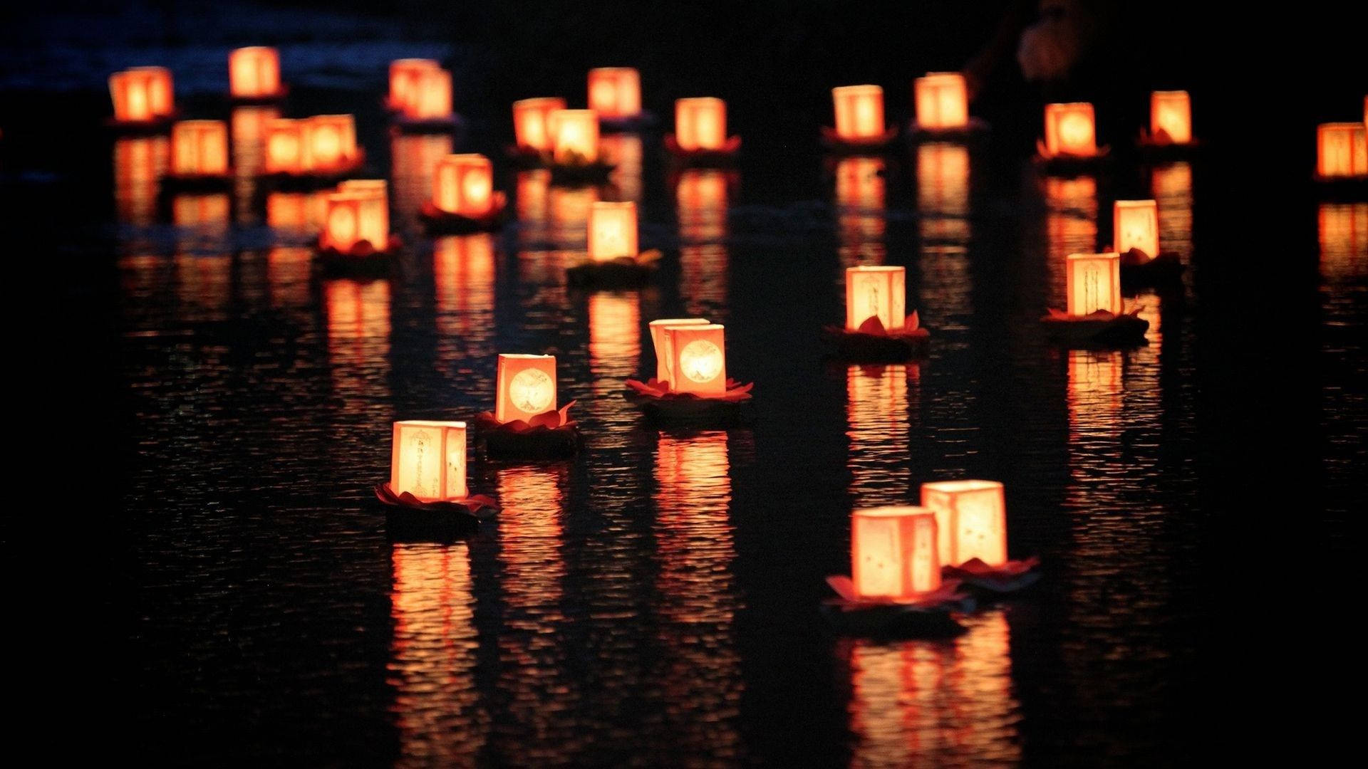 Light 桌布 壁紙 — 發光的紙燈籠在黑暗的水面上寧靜地漂浮，反射出溫暖的橙色光芒，營造出寧靜的夜景。