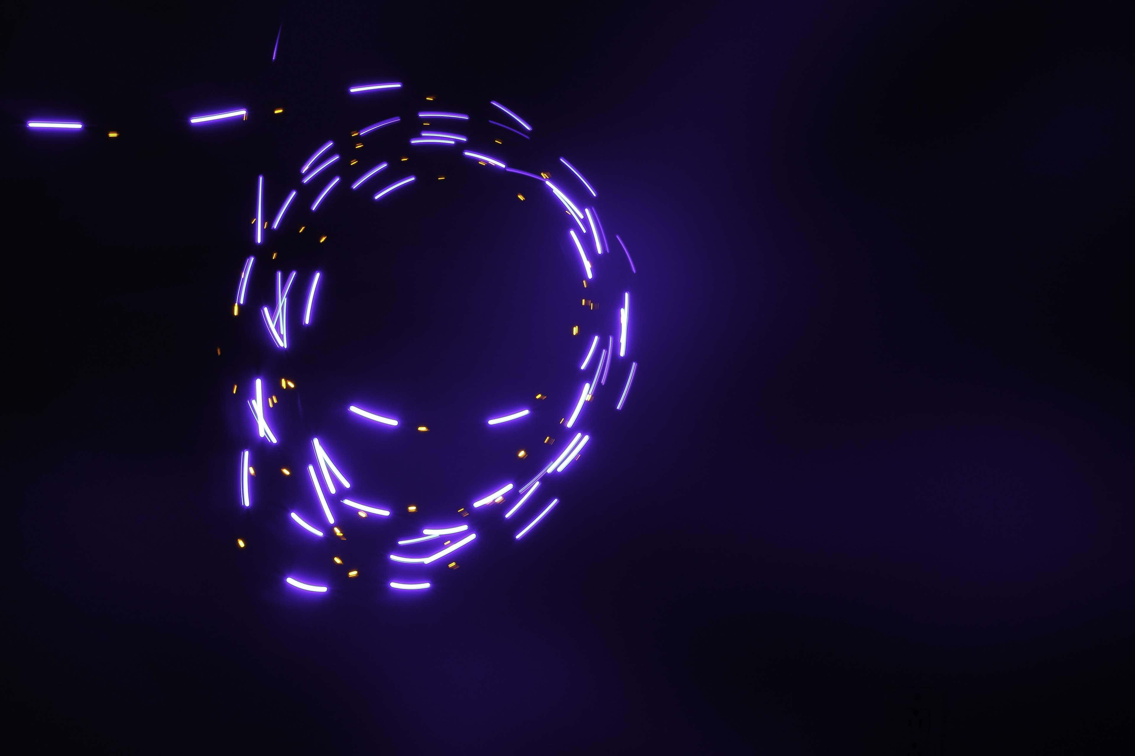 LED 桌布 壁紙 — 發光的紫色和黃色光跡在黑暗背景上形成旋轉的螺旋。