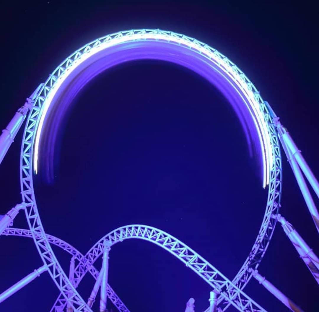 Roller Coaster 桌布 壁紙 — 發光的紫色雲霄飛車環圈在黑暗夜空下因運動而模糊。