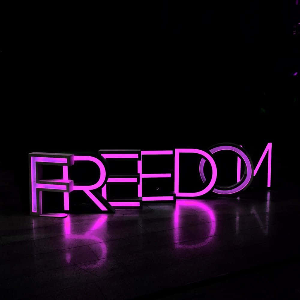 Neon Lights Aesthetic 桌布 壁紙 — 發光的紫色霓虹燈字母拼出自由，在昏暗的空間中，在深色拋光地板上投射出鮮豔的倒影。