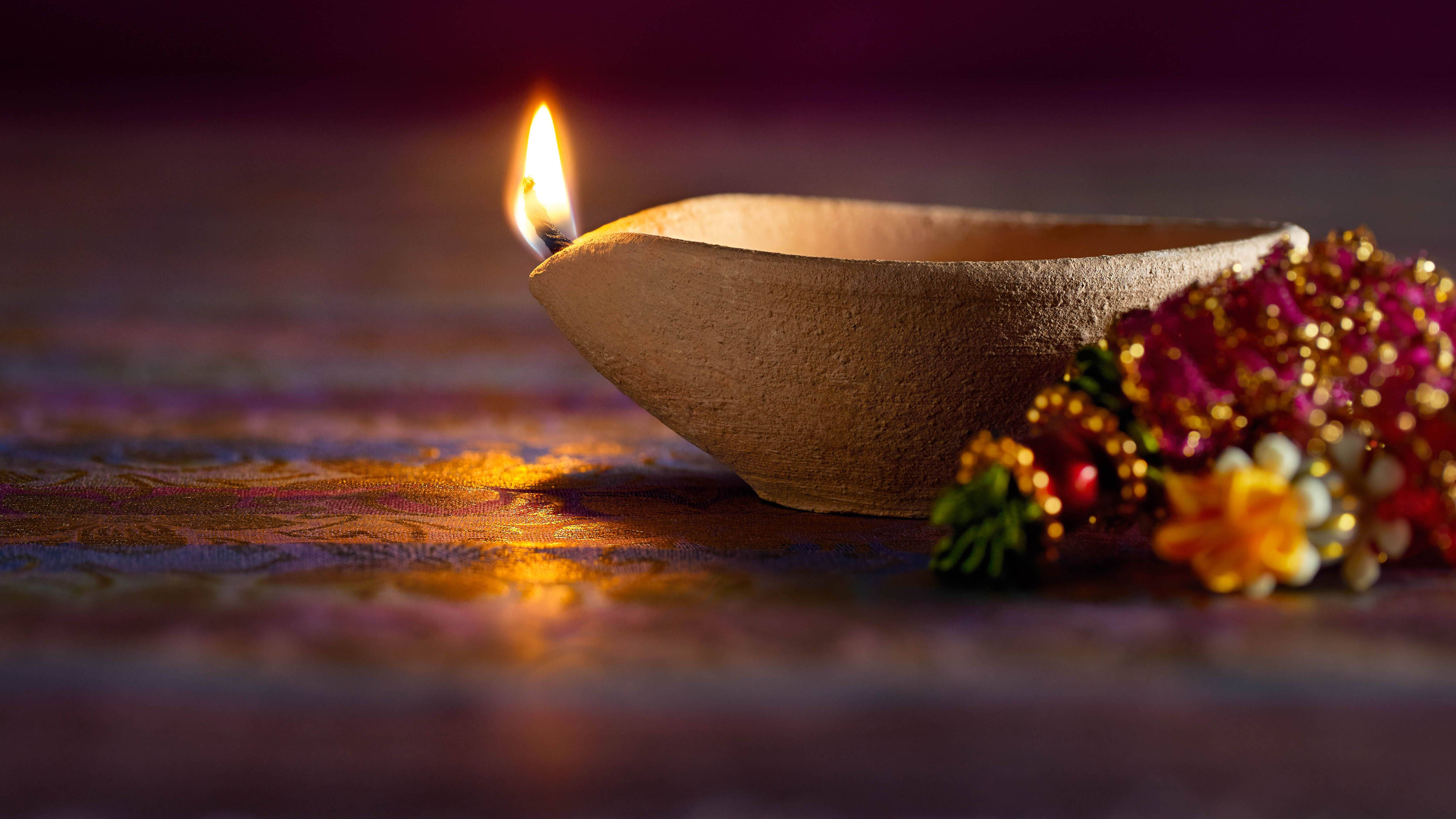Happy Diwali 桌布 壁紙 — 發光的迪亞蠟燭在圖案表面旁邊的彩色花環上投射出溫暖的光芒。