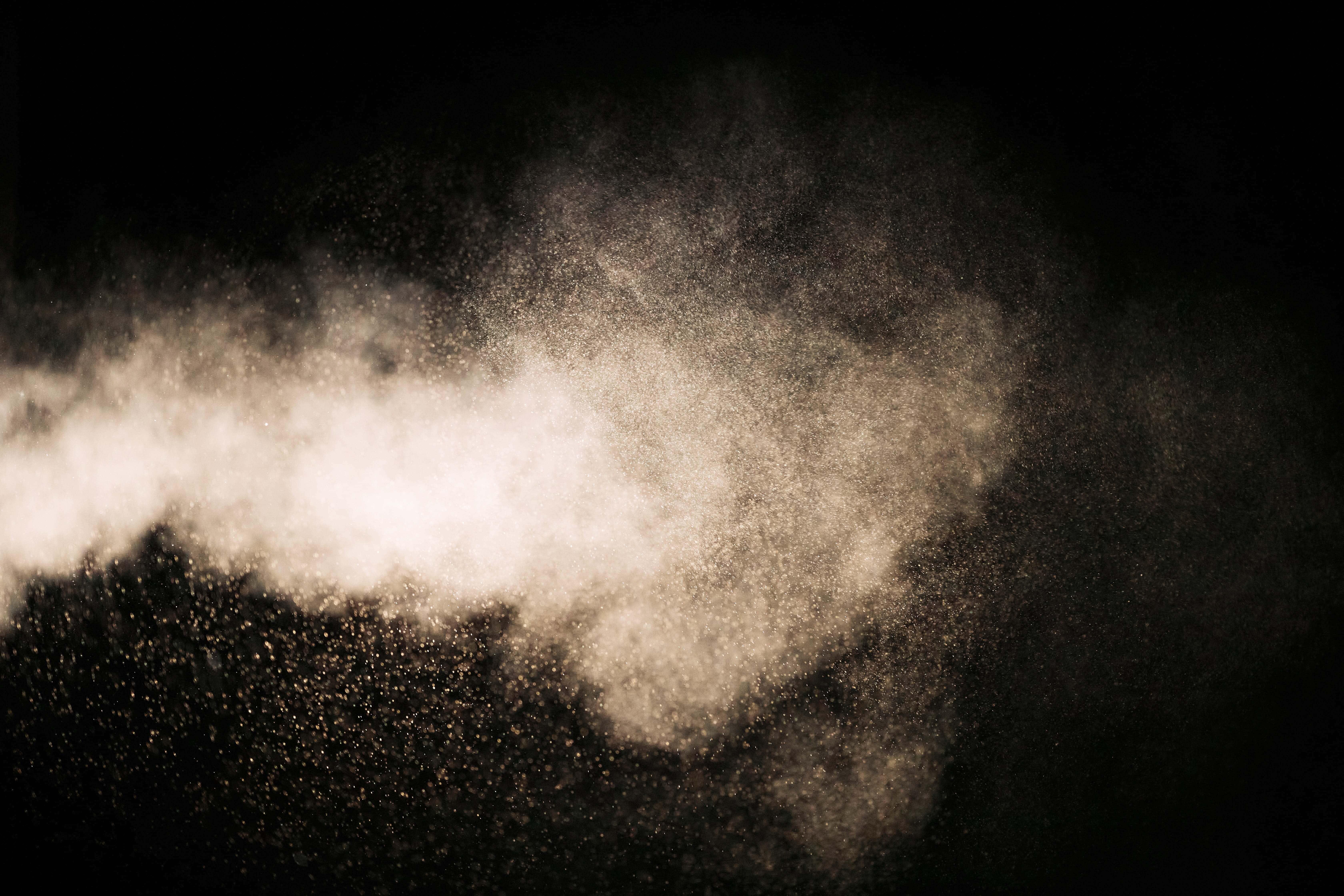 Dust 桌布 壁紙 — 發光的金色塵埃粒子動態爆發，在純黑背景上綻放。