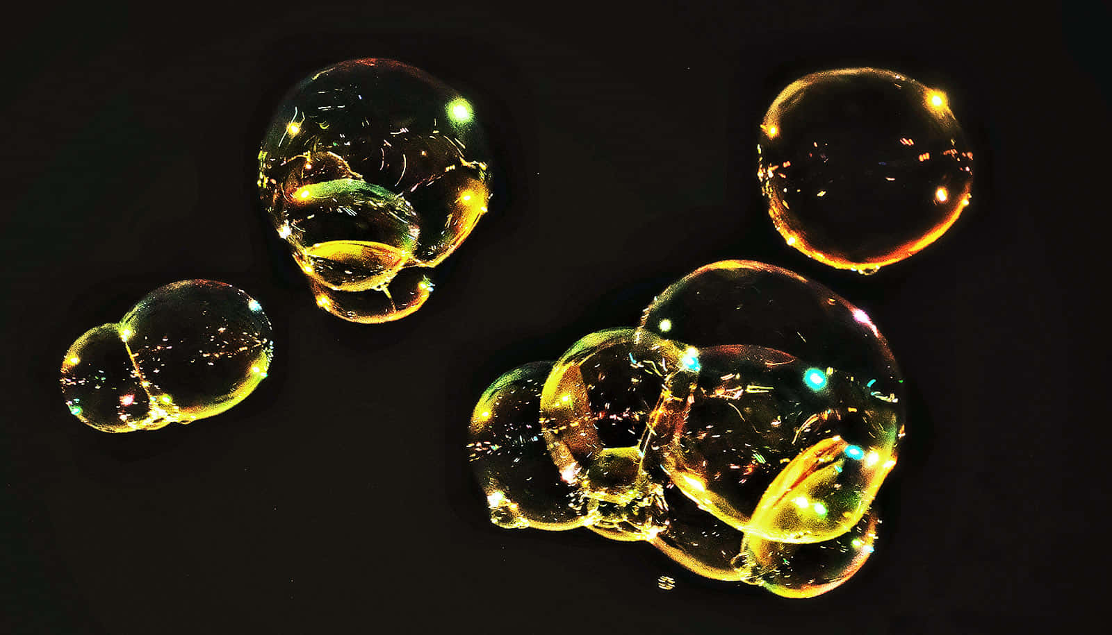 Bubble 桌布 壁紙 — 發光的金色氣泡在深黑色背景上漂浮，在其半透明球體內反射出五彩繽紛的光芒。