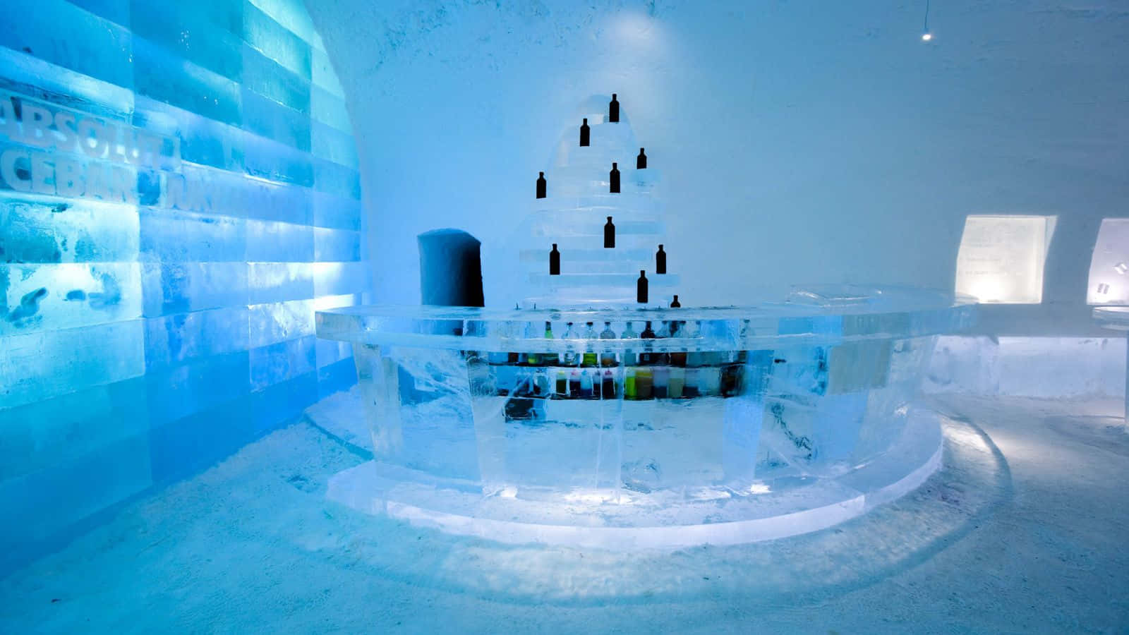 Ice Hotel 桌布 壁紙 — 發光藍色冰吧，雕刻牆壁，中央冰櫃在涼爽環境燈光下放置瓶子。