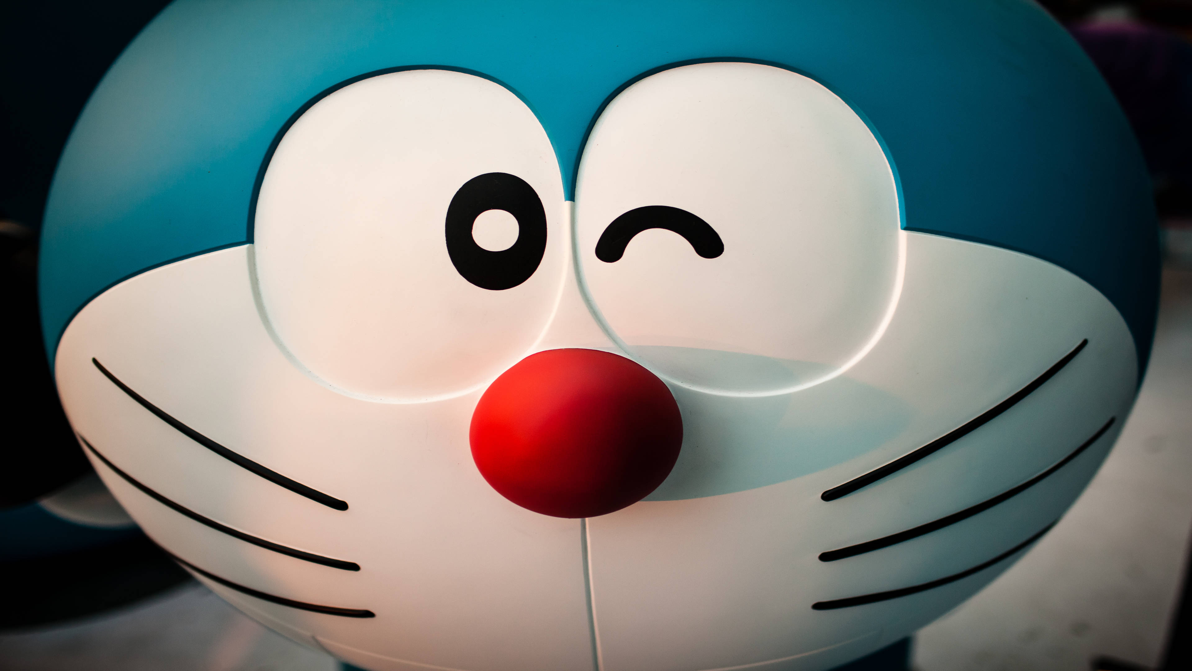 Doraemon 桌布 壁紙 — 發光藍色機器貓的特寫，有一隻眼睛在眨眼，紅色的鼻子。