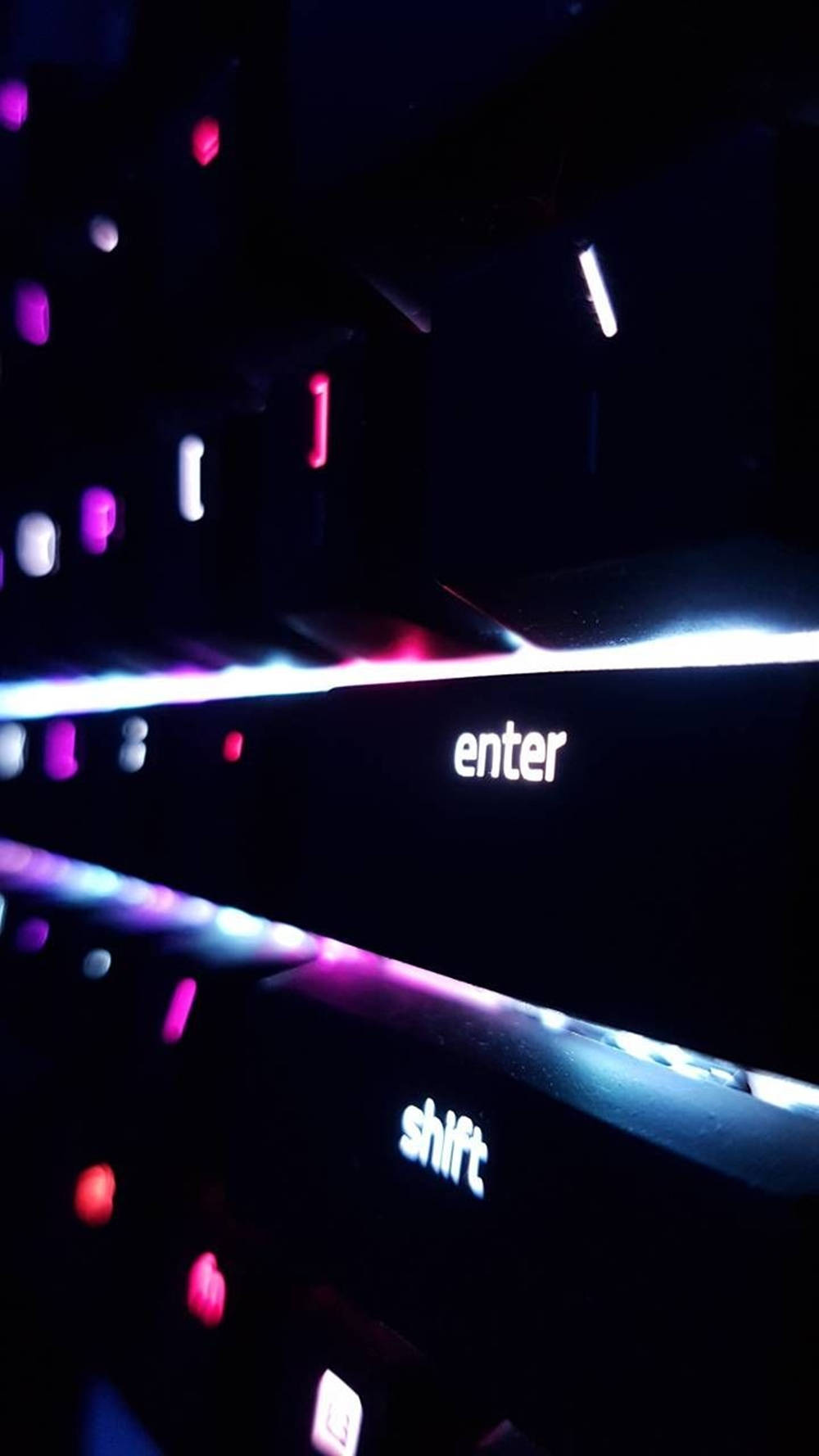 鍵盤 桌布 壁紙 — 發光鍵盤的 Enter 和 Shift 鍵特寫，在深色背景上沐浴在充滿活力的紫色和藍色背光中。
