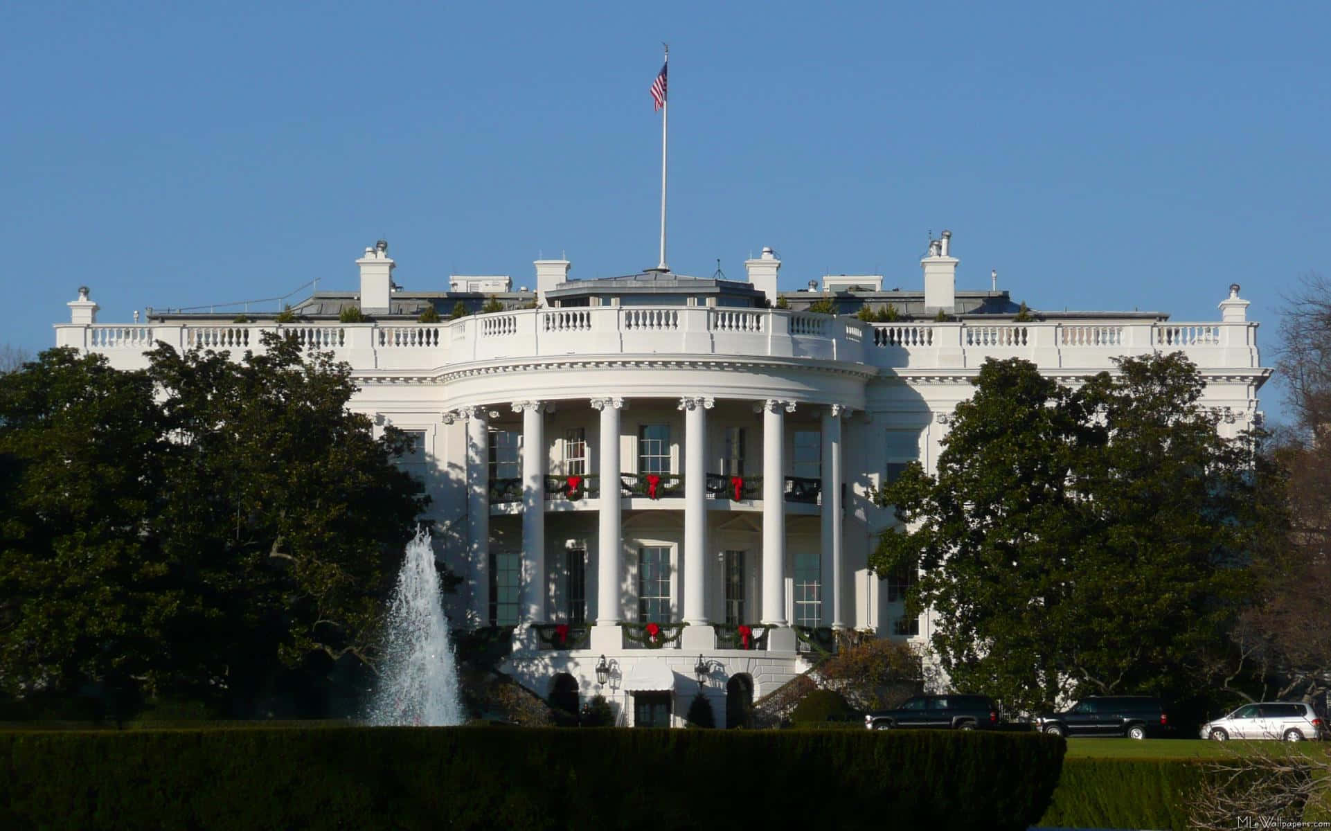 white house 桌布 壁紙 — 白宮在晴朗的藍天下雄偉地矗立，前面有節日紅色的花環和噴水的噴泉。
