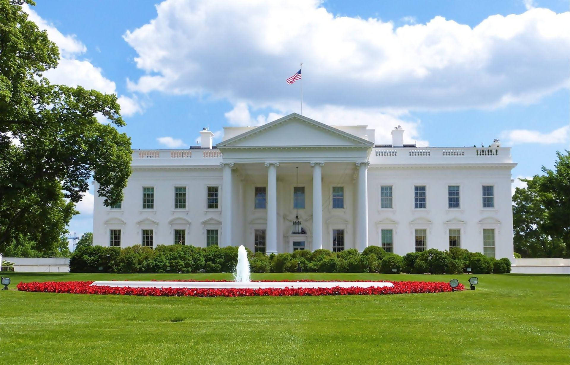 Washington 桌布 壁紙 — 白宮在晴朗的藍天白雲下雄偉地矗立，周圍環繞著鬱鬱蔥蔥的綠色草坪和充滿活力的紅色花壇。